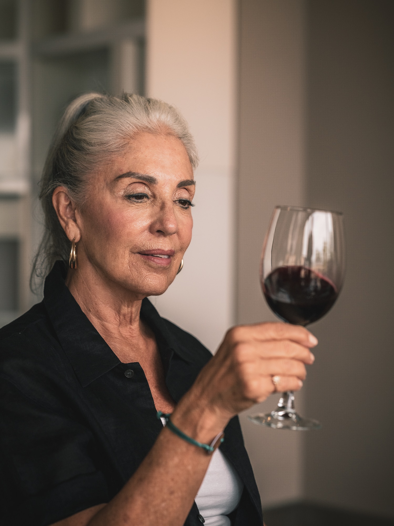 Mature woman with gray hair holding a glass of red wine.