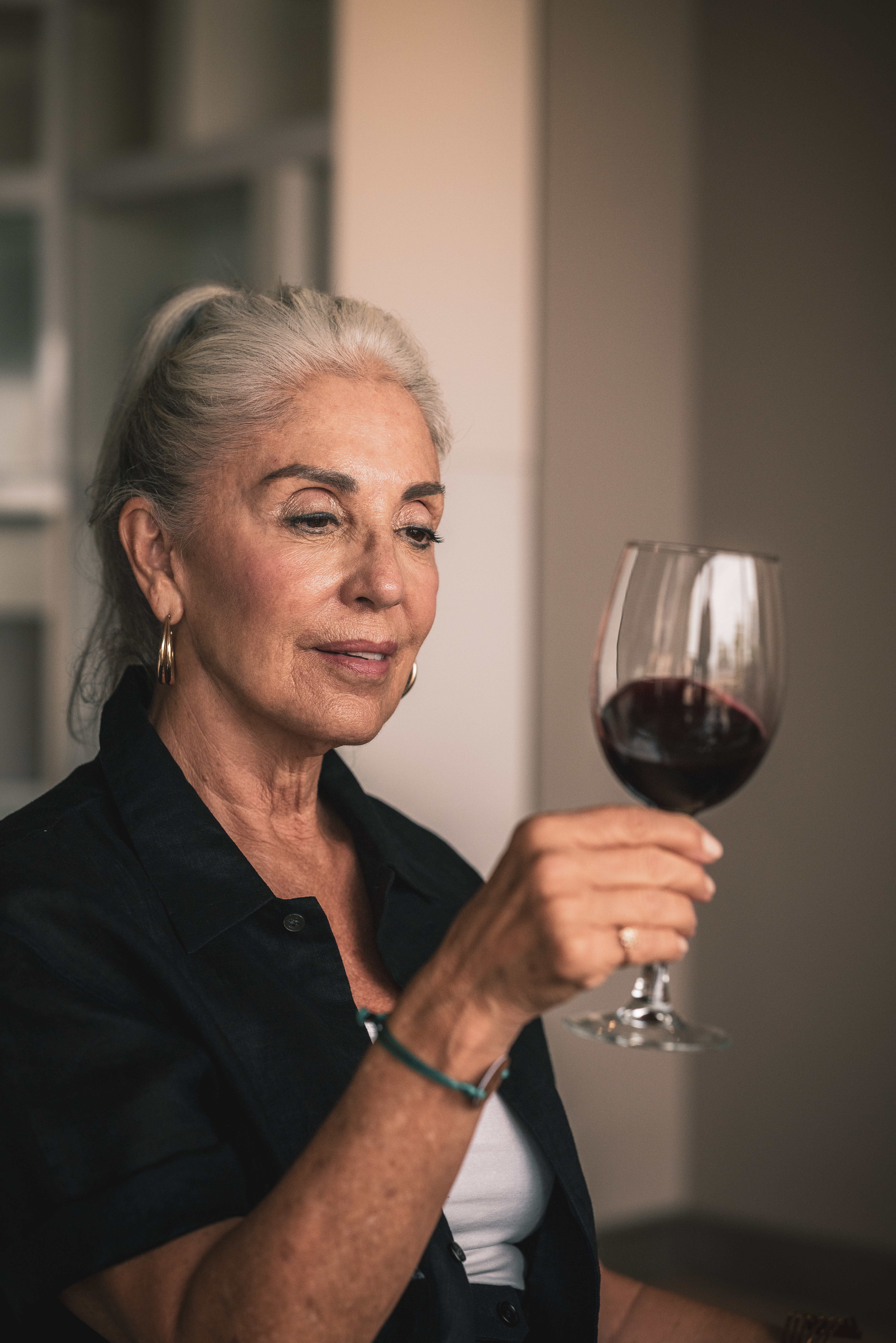 Mature woman with gray hair holding a glass of red wine.
