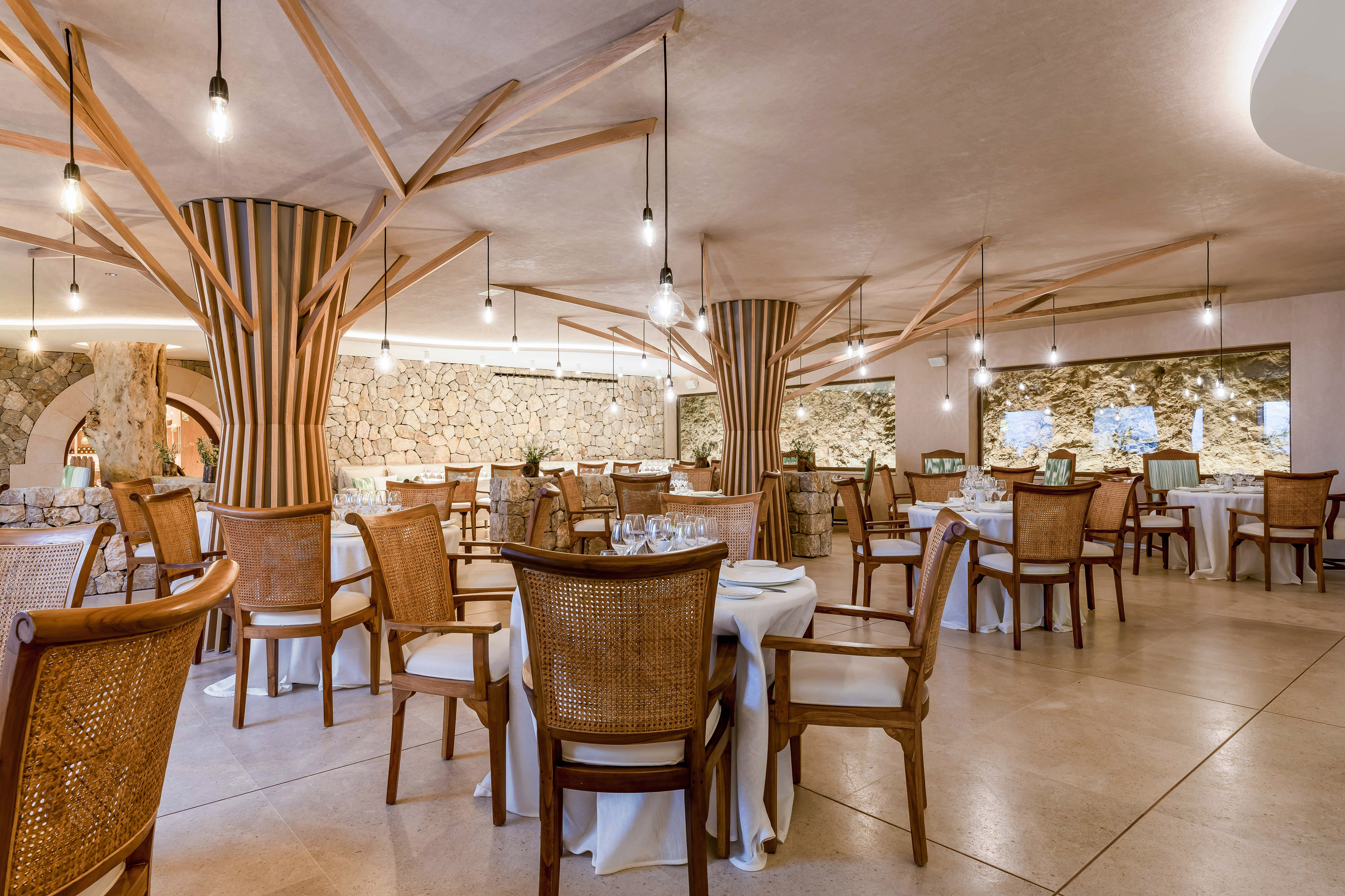 Elegant restaurant: tree-like wooden pillars, stone walls, and wicker chairs.