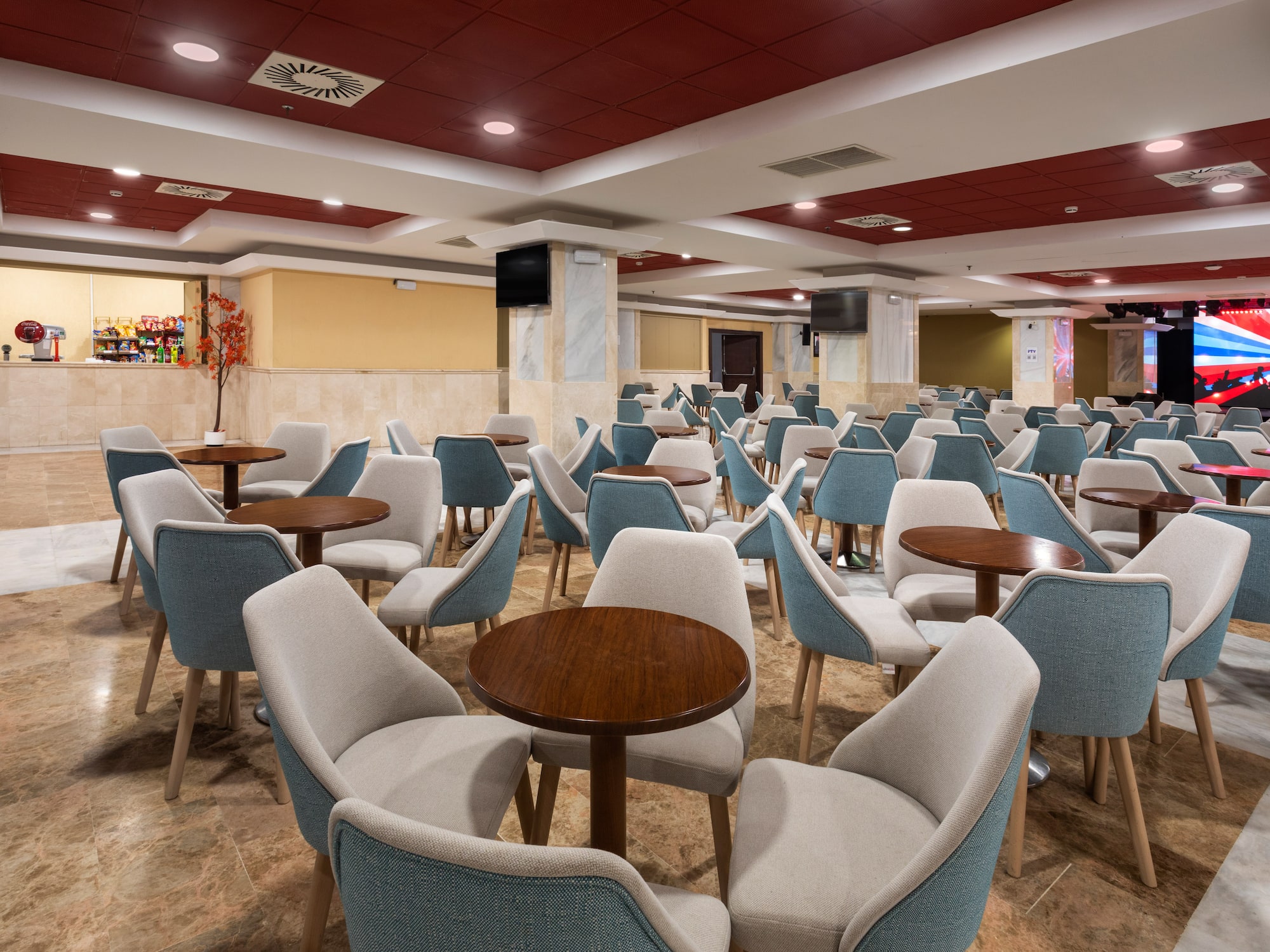 Modern hotel event space with blue-beige chairs, round tables, snack bar.
