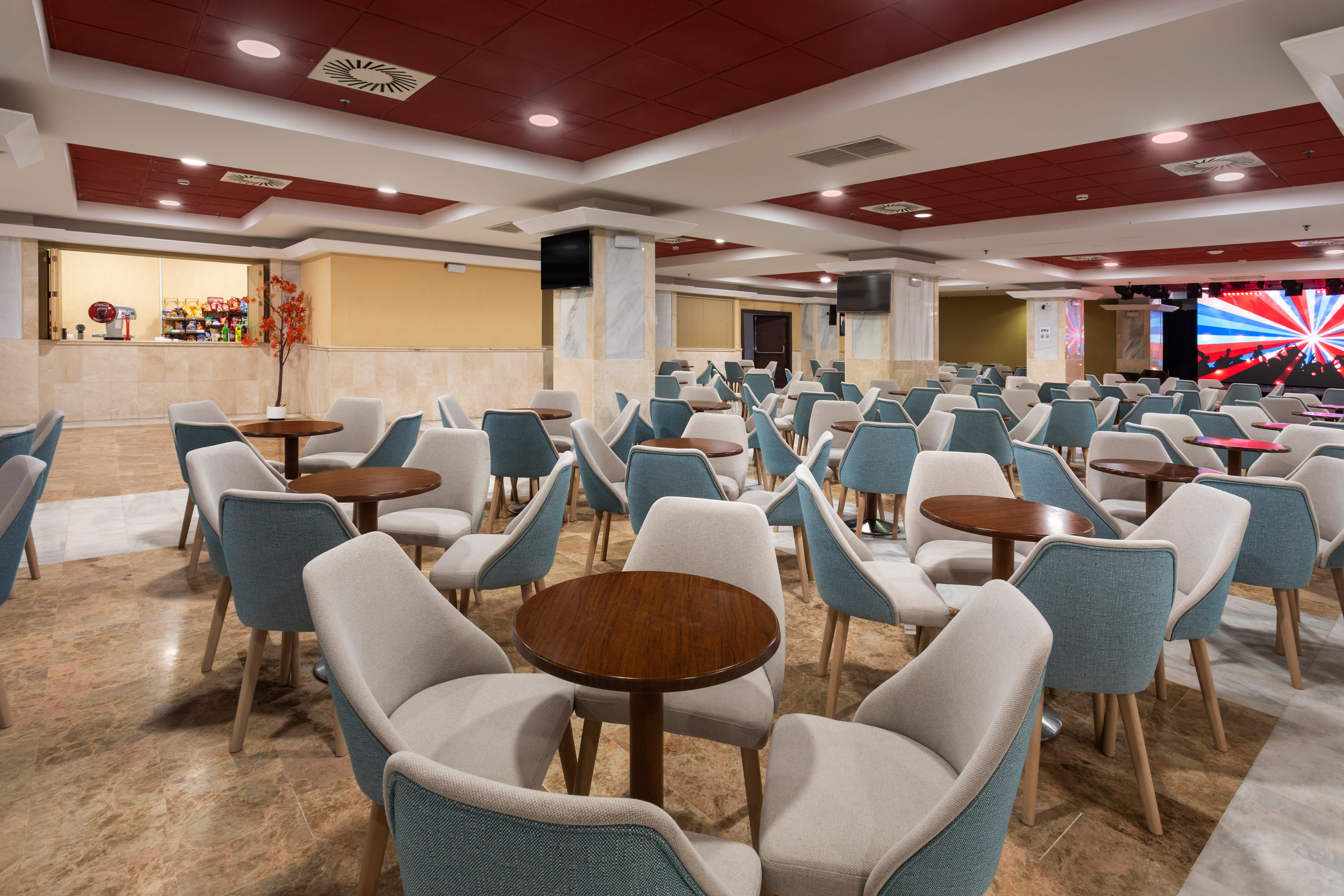 Modern hotel event space with blue-beige chairs, round tables, snack bar.