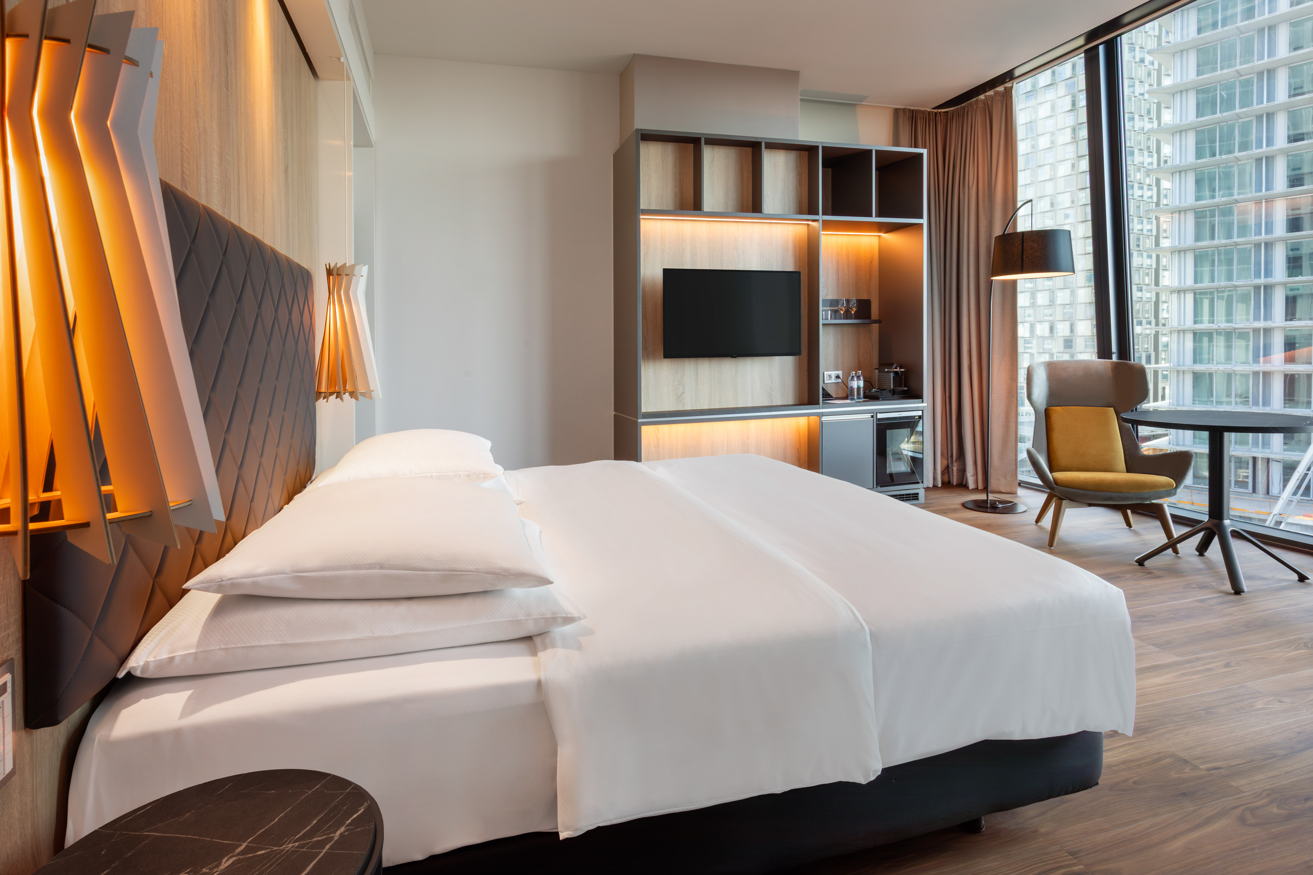 Stylish hotel room featuring a king bed, city skyline view, TV, and cozy seating area.