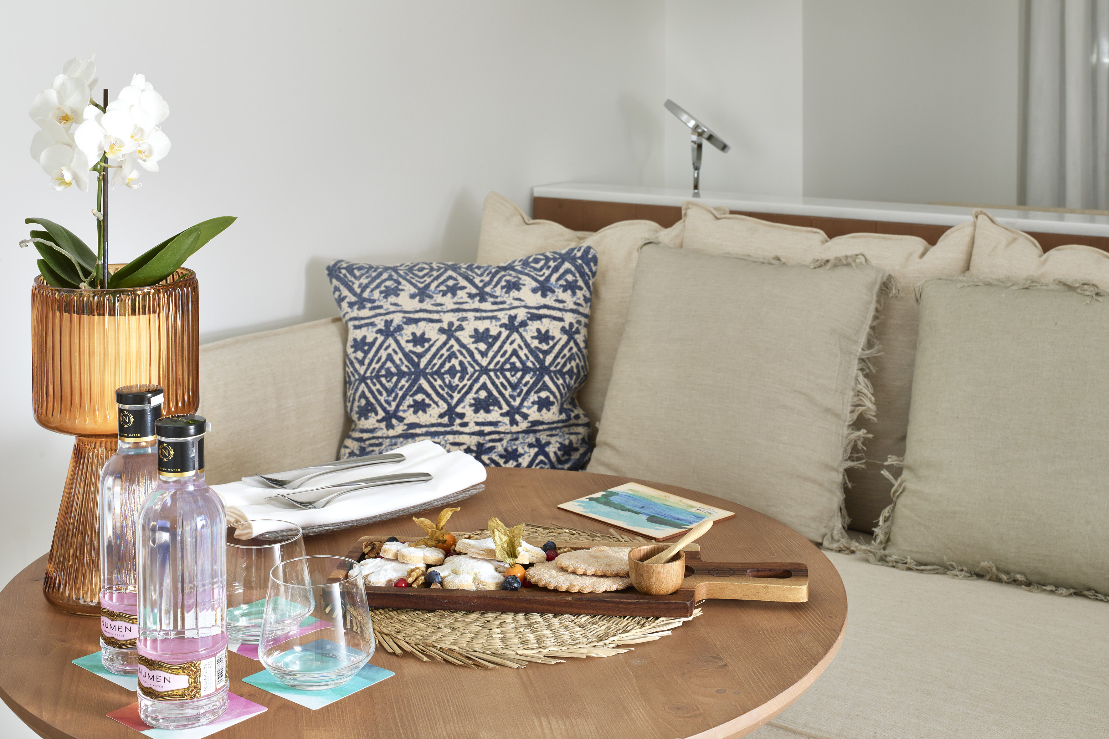 Hotel welcome snacks, water, and orchid on a wooden table.