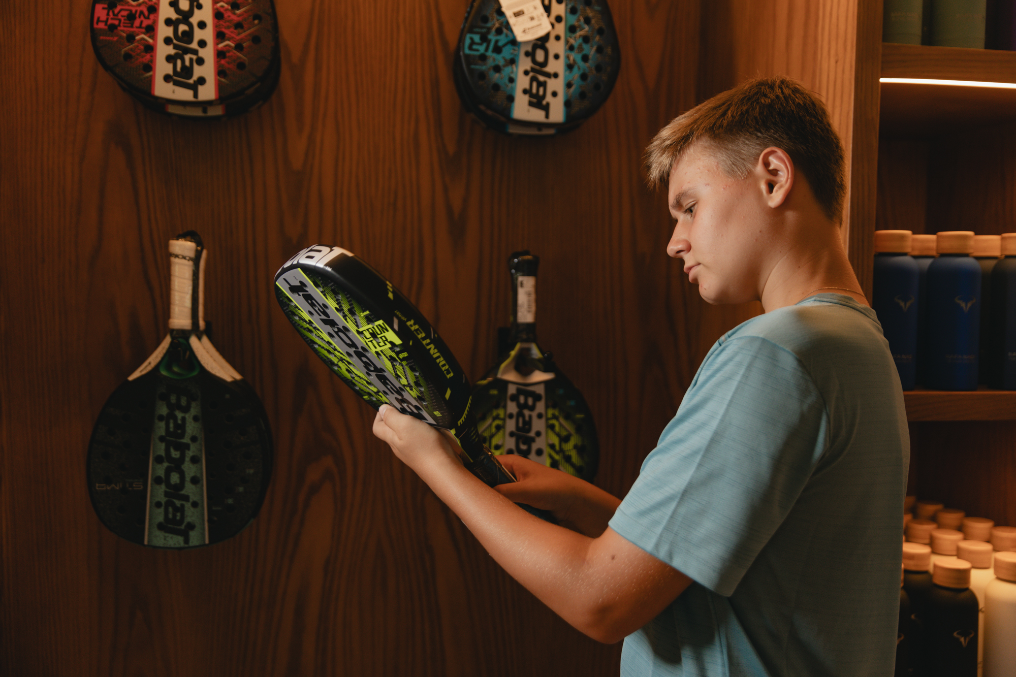 Teenager choosing a neon green padel racket in a sports equipment shop.