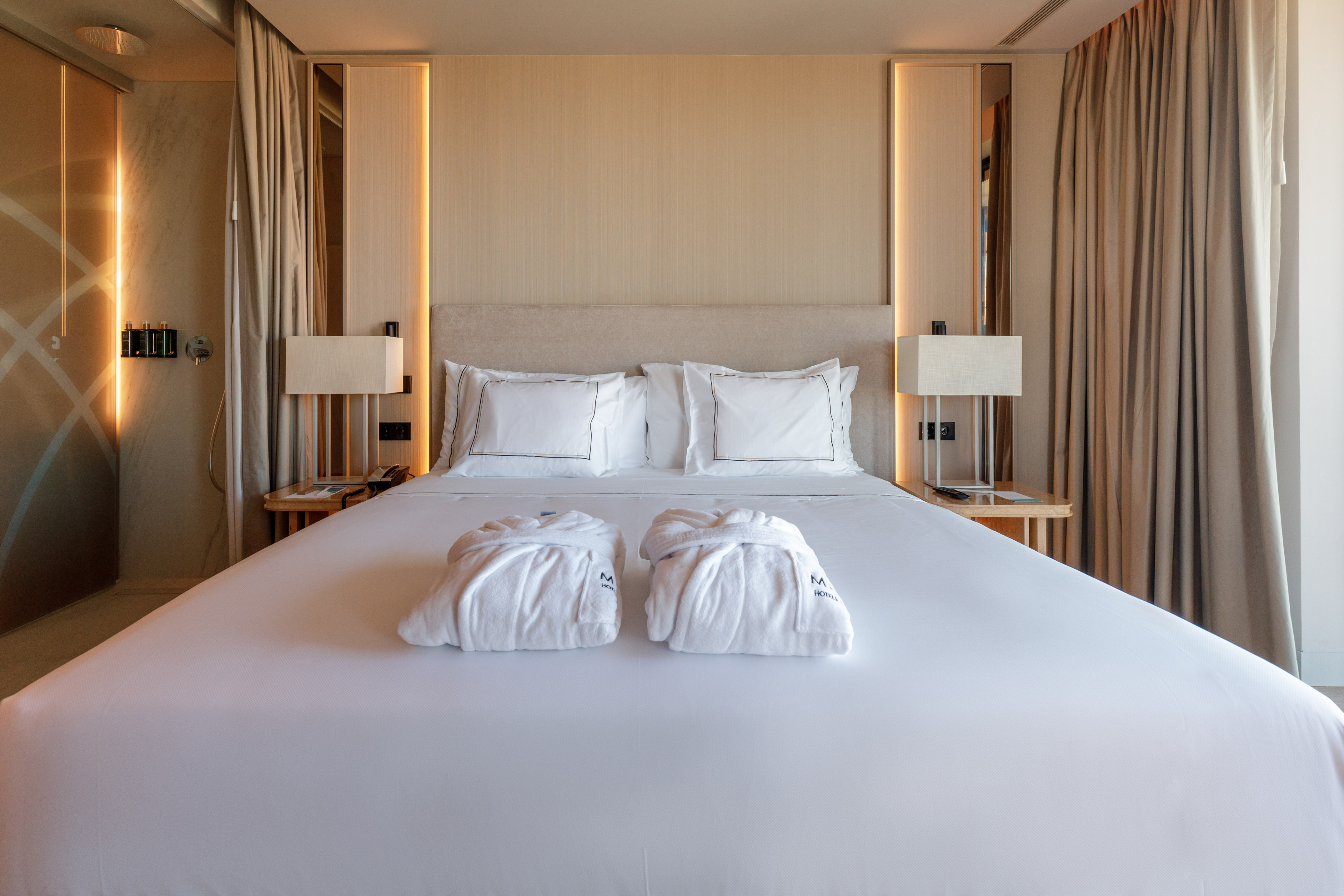 Luxury hotel bedroom with king bed, white bedding, and two bathrobes.