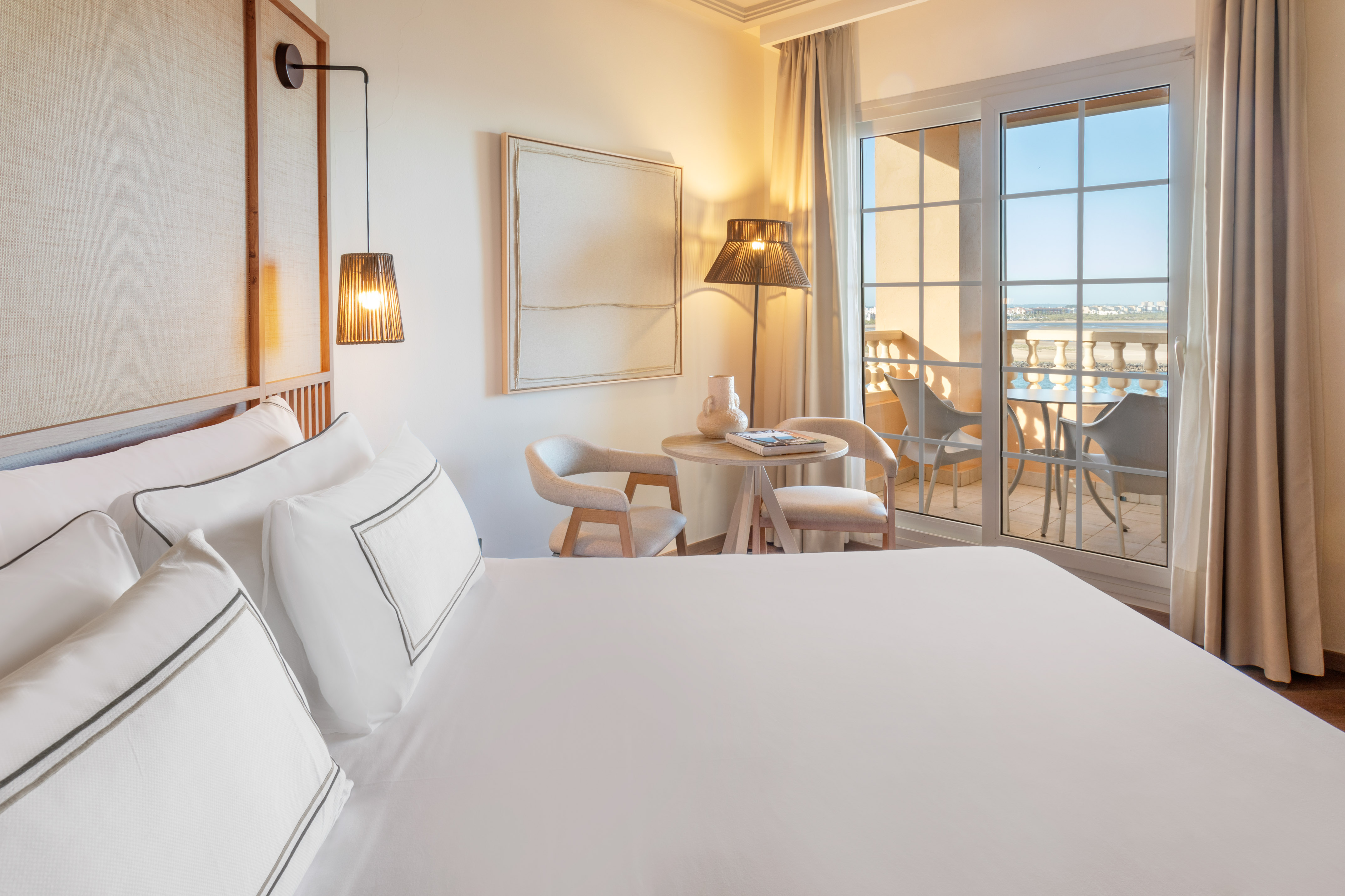 Luxurious hotel bedroom with white linens, balcony, and scenic sea view.