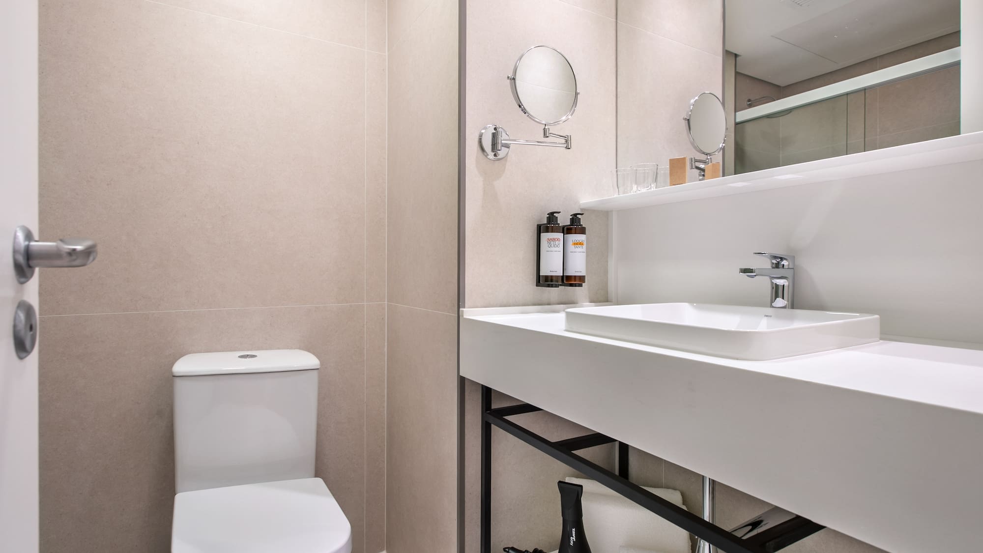 Modern hotel bathroom with white toilet, vanity sink, mirror, and neutral decor.