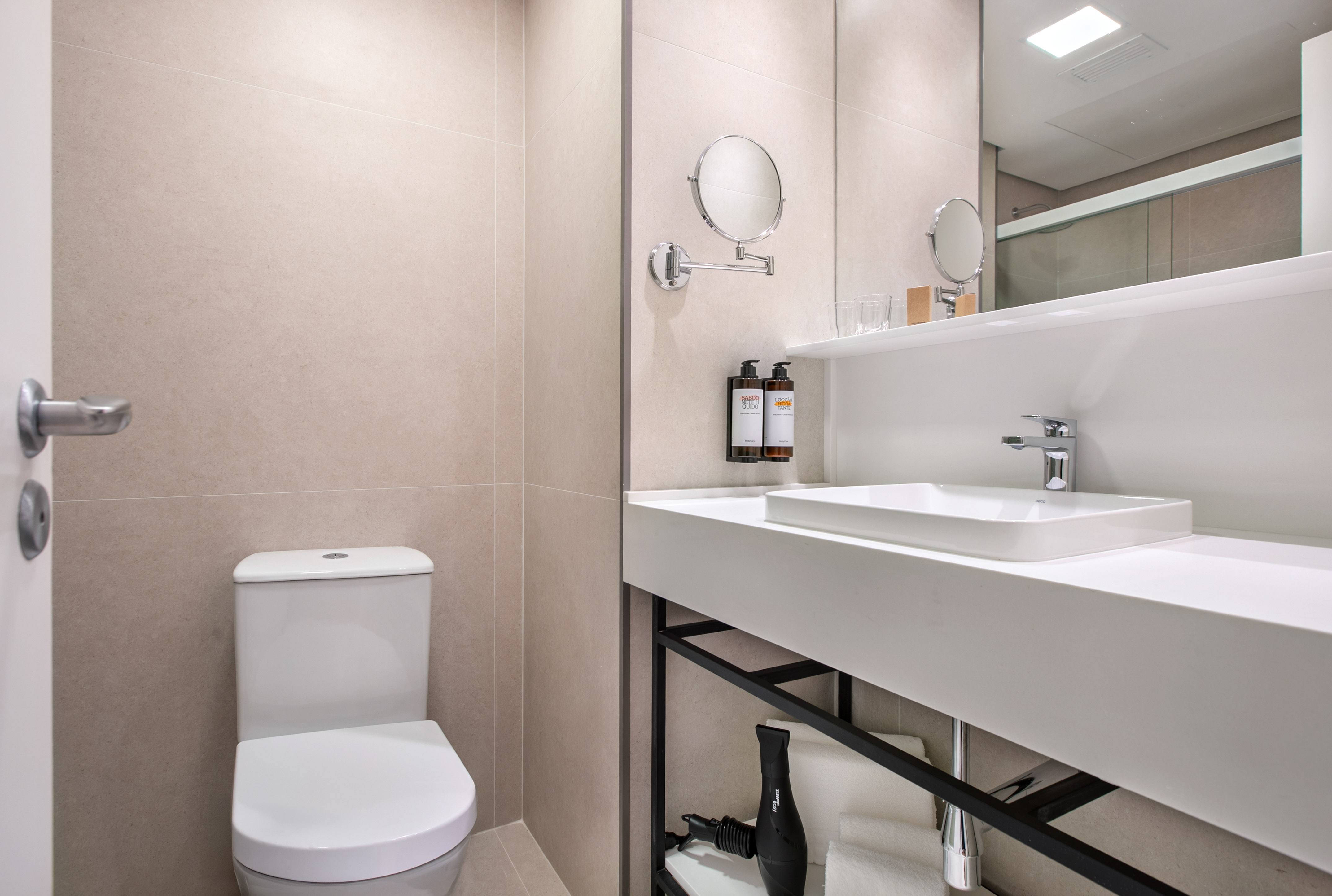 Modern hotel bathroom with white toilet, vanity sink, mirror, and neutral decor.