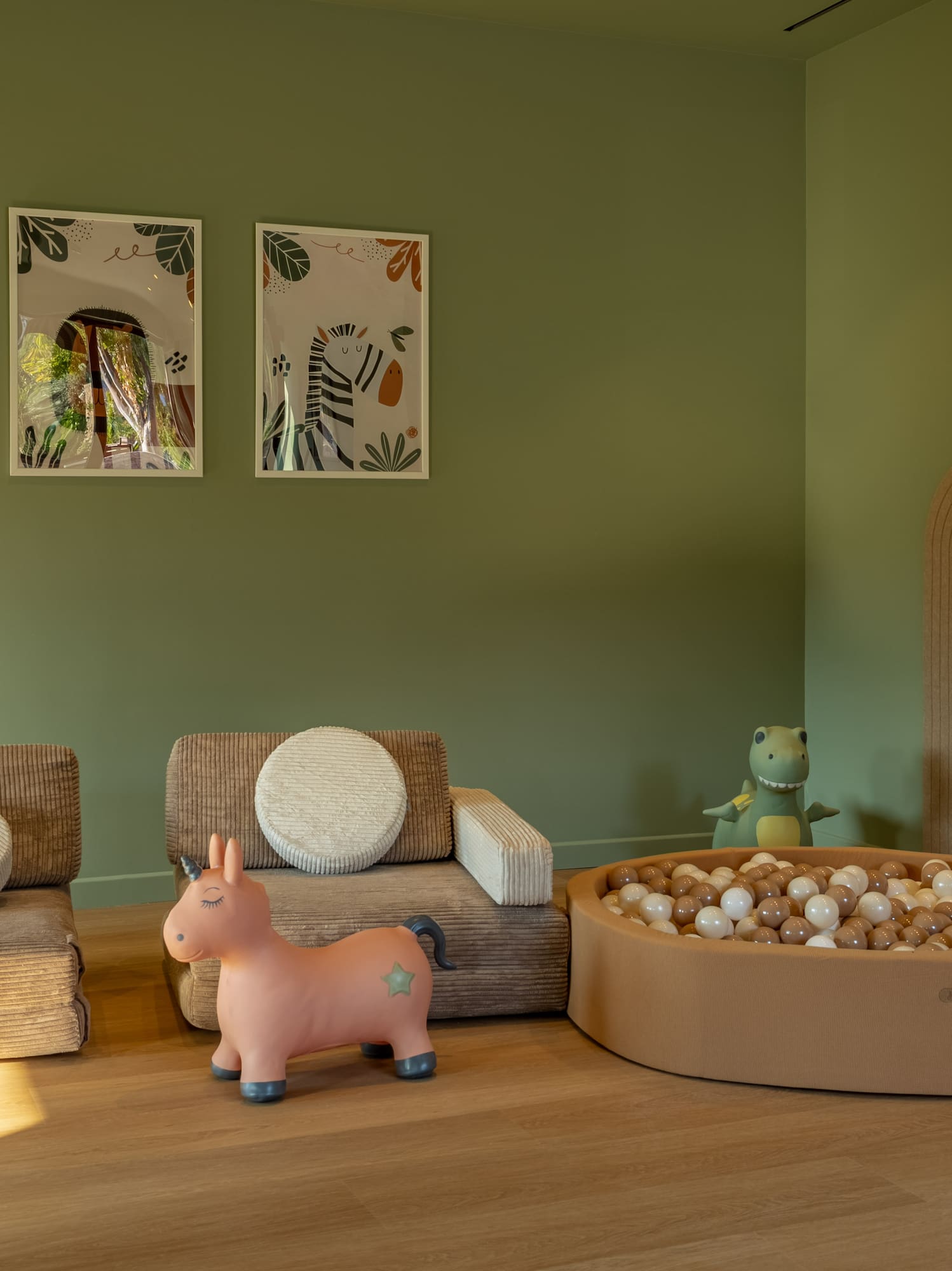 Child's playroom with ball pit, corduroy chairs, unicorn toy, and jungle art.