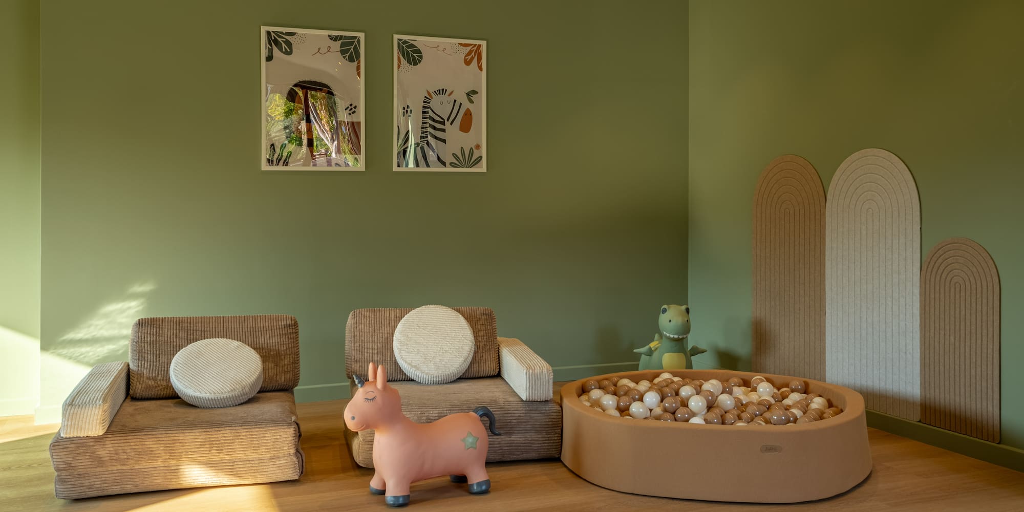 Green kids' play room with ball pit, unicorn bouncer, and modular seating.