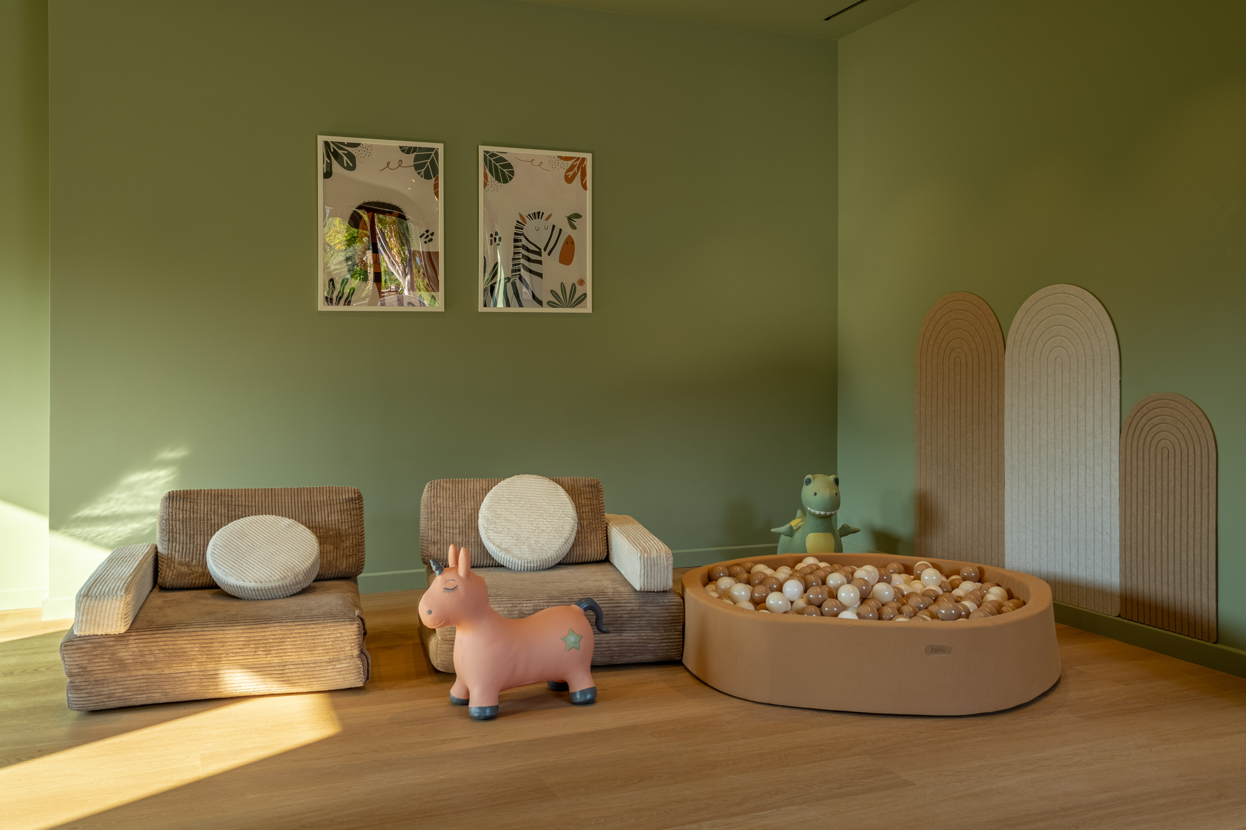 Child's playroom with ball pit, corduroy chairs, unicorn toy, and jungle art.