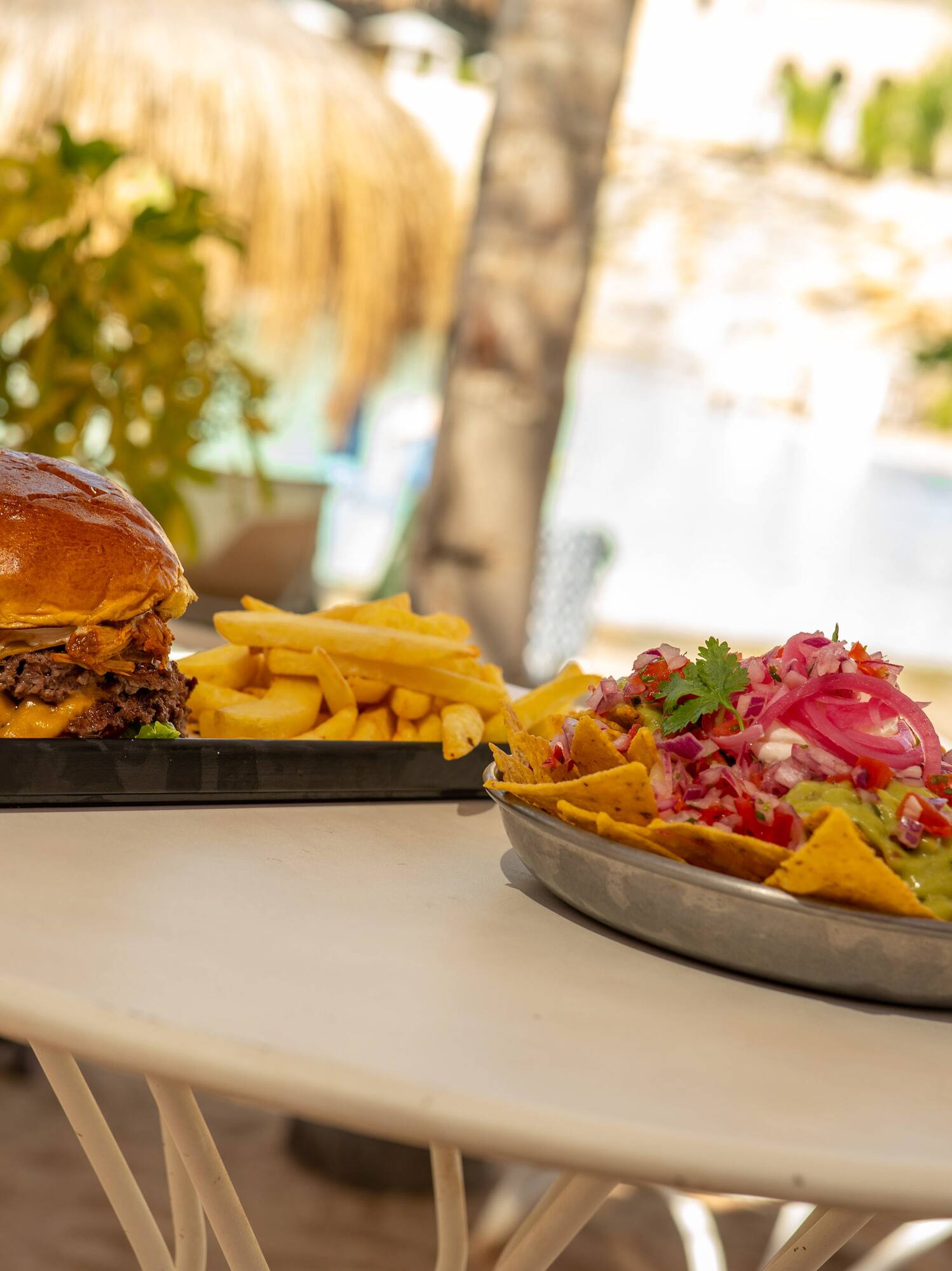Tropical outdoor dining: cheeseburger, fries, and loaded nachos.