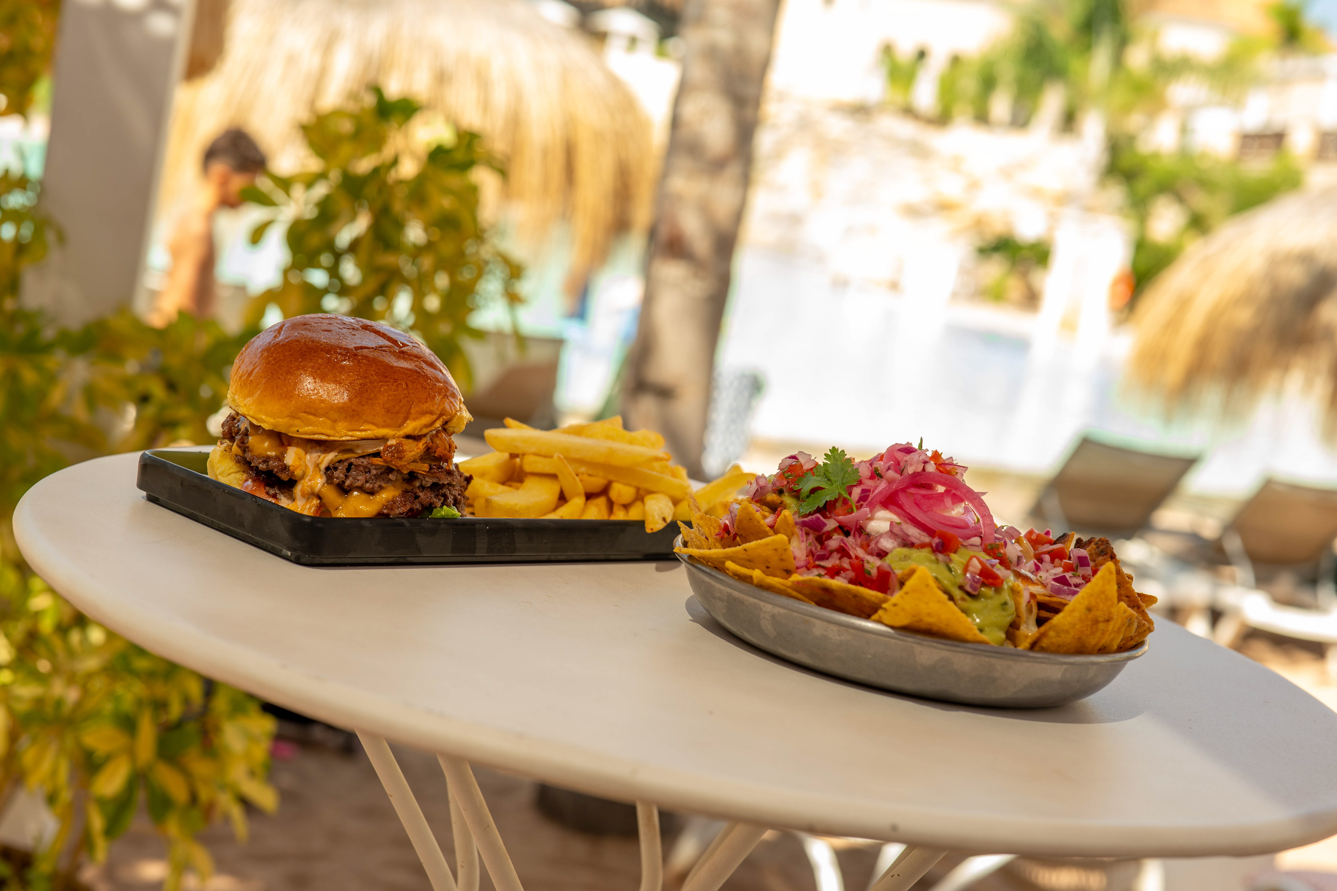 Tropical outdoor dining: cheeseburger, fries, and loaded nachos.