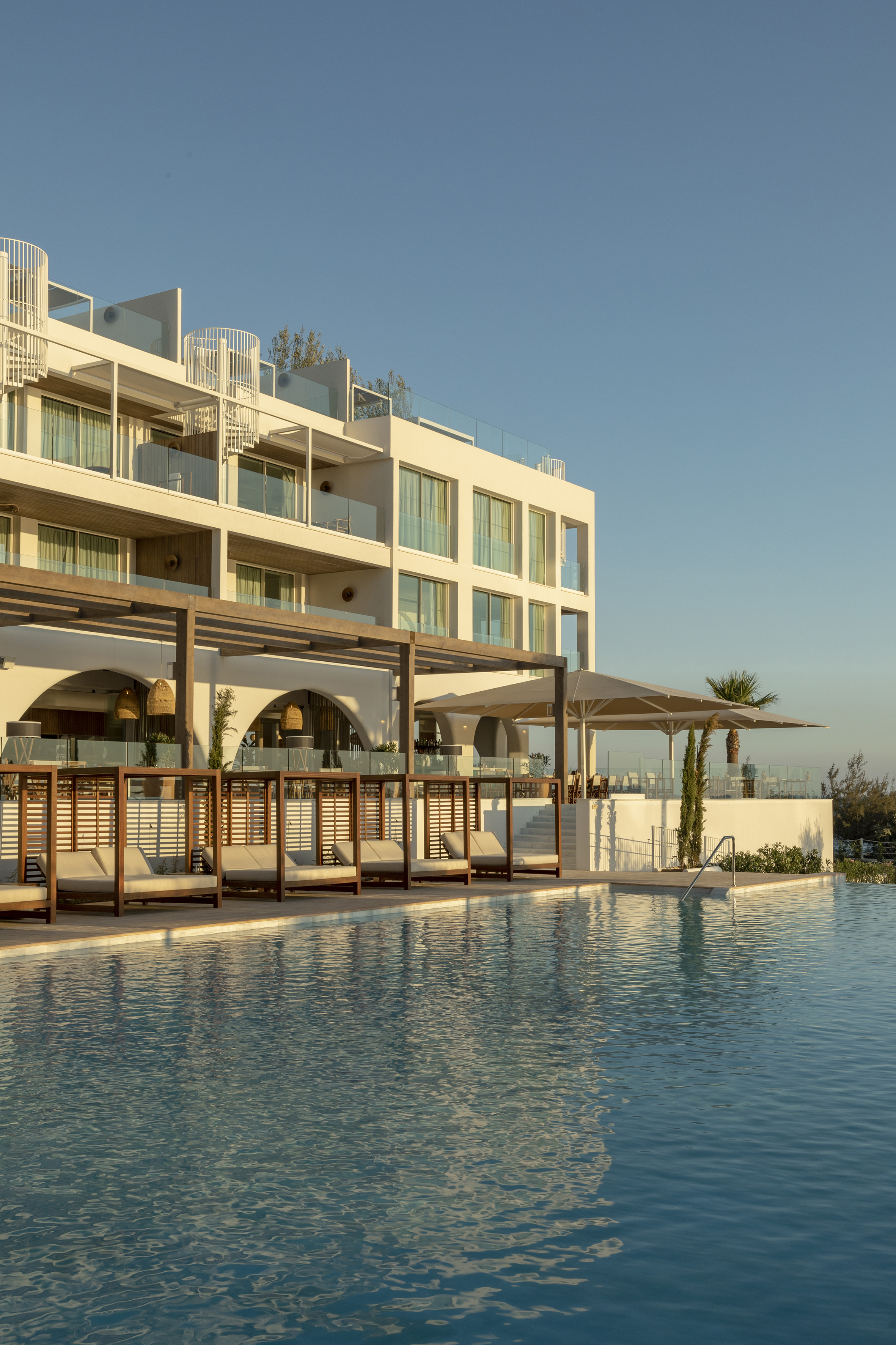 Modern luxury hotel with blue swimming pool, cabanas, and sunlit architecture.