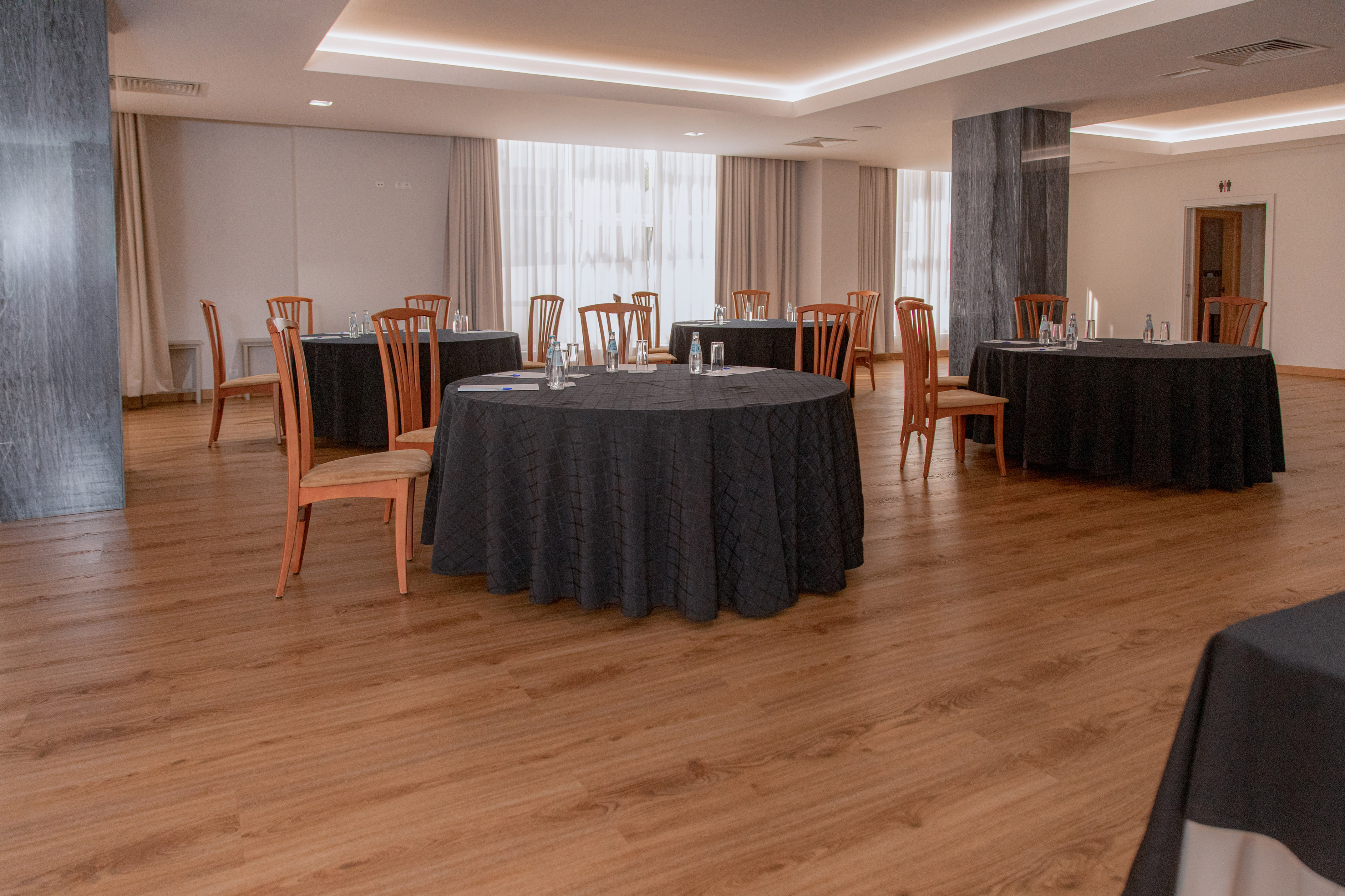 Hotel meeting room with round tables, black tablecloths, and wooden chairs.
