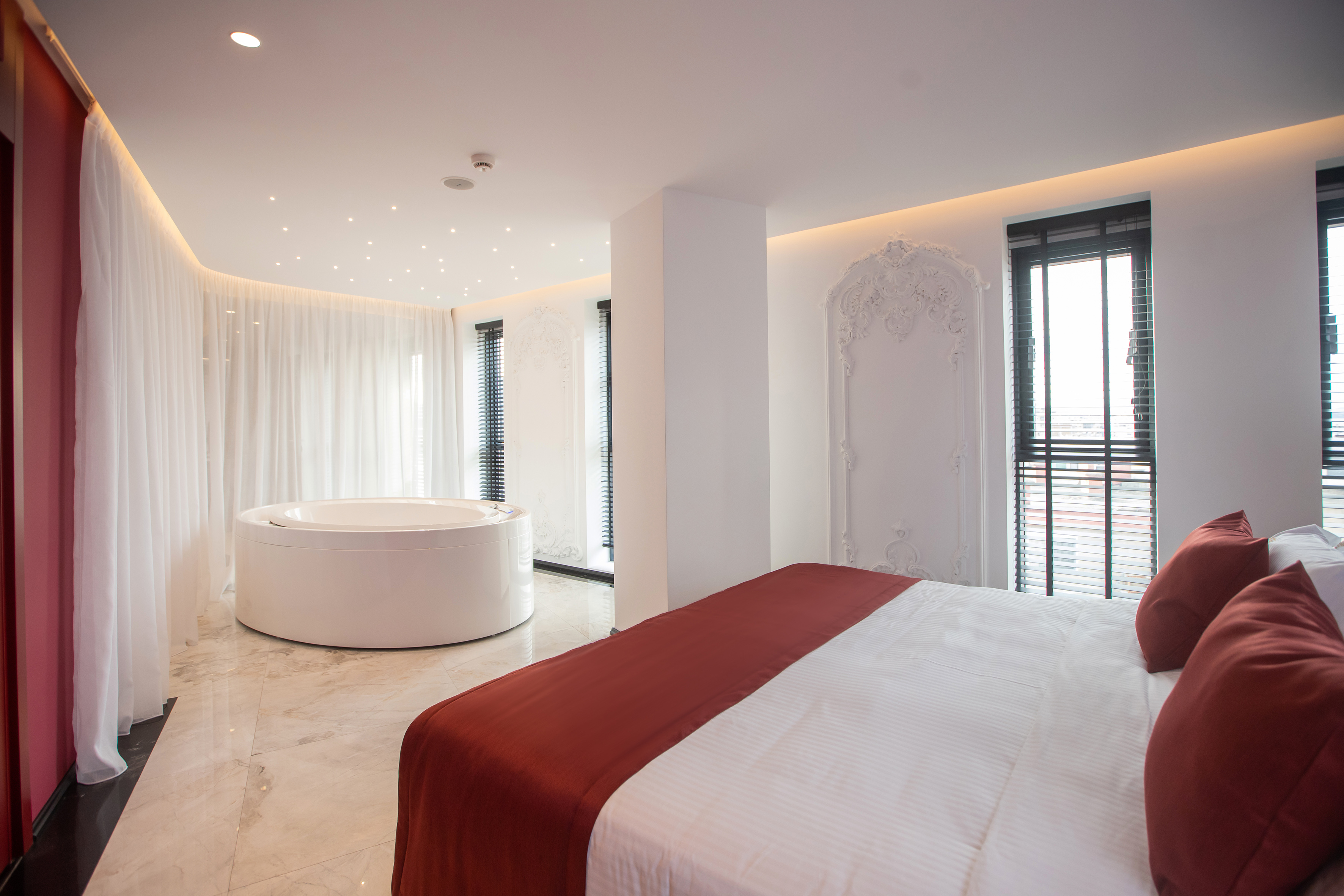 Luxury hotel suite with modern bed, round jacuzzi, and elegant interior.
