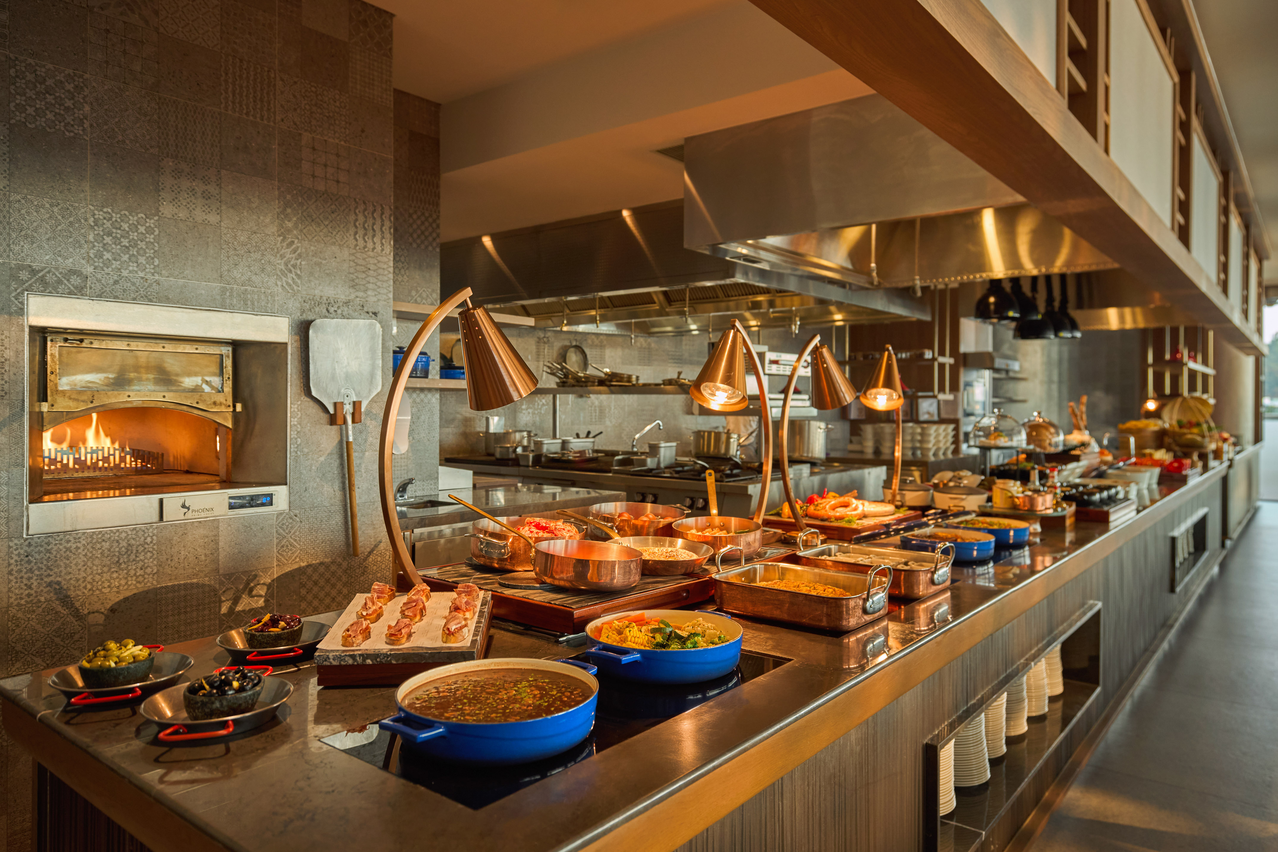 Modern buffet with hot food, wood-fired oven, and prepared dishes in a restaurant.