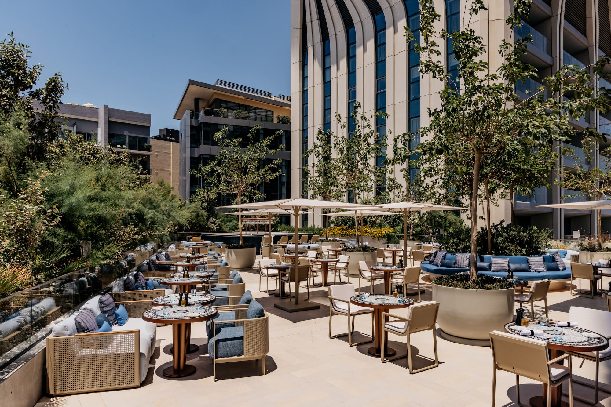 Modern outdoor restaurant patio with stylish seating, umbrellas, and green trees.