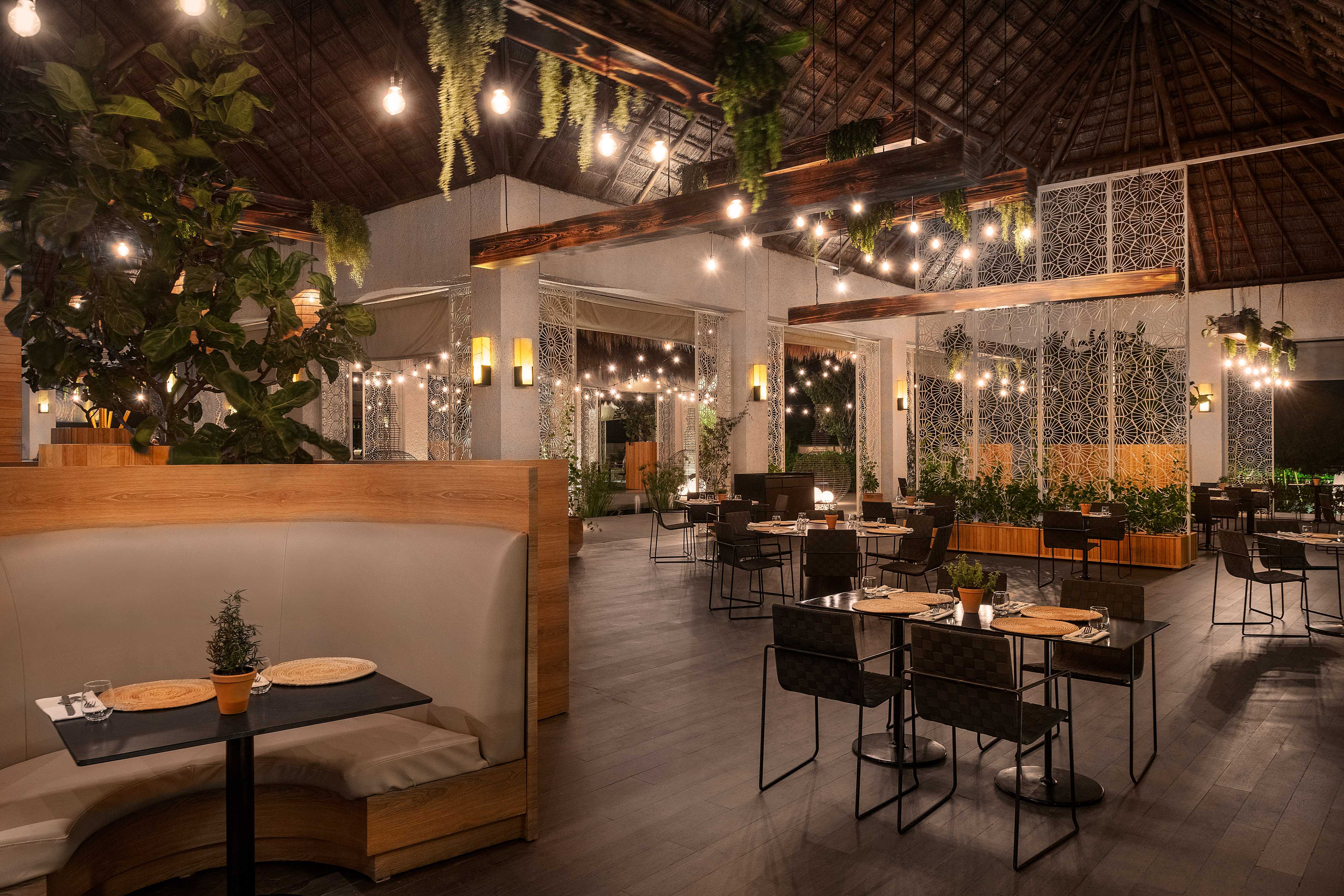 Tropical restaurant interior with string lights, lush plants, and thatched roof.
