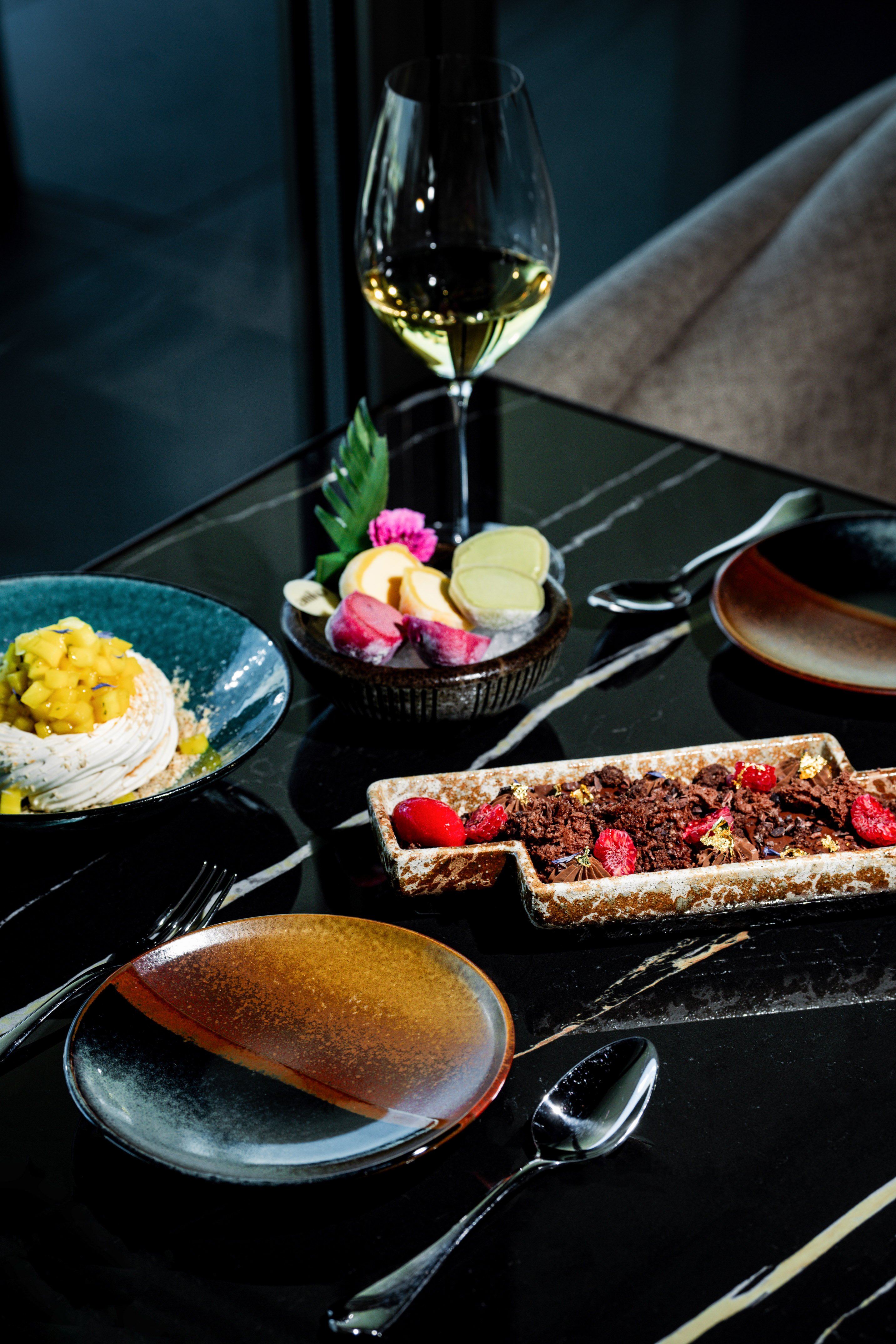 Gourmet desserts: mango meringue, chocolate, mochi, white wine on marble table.