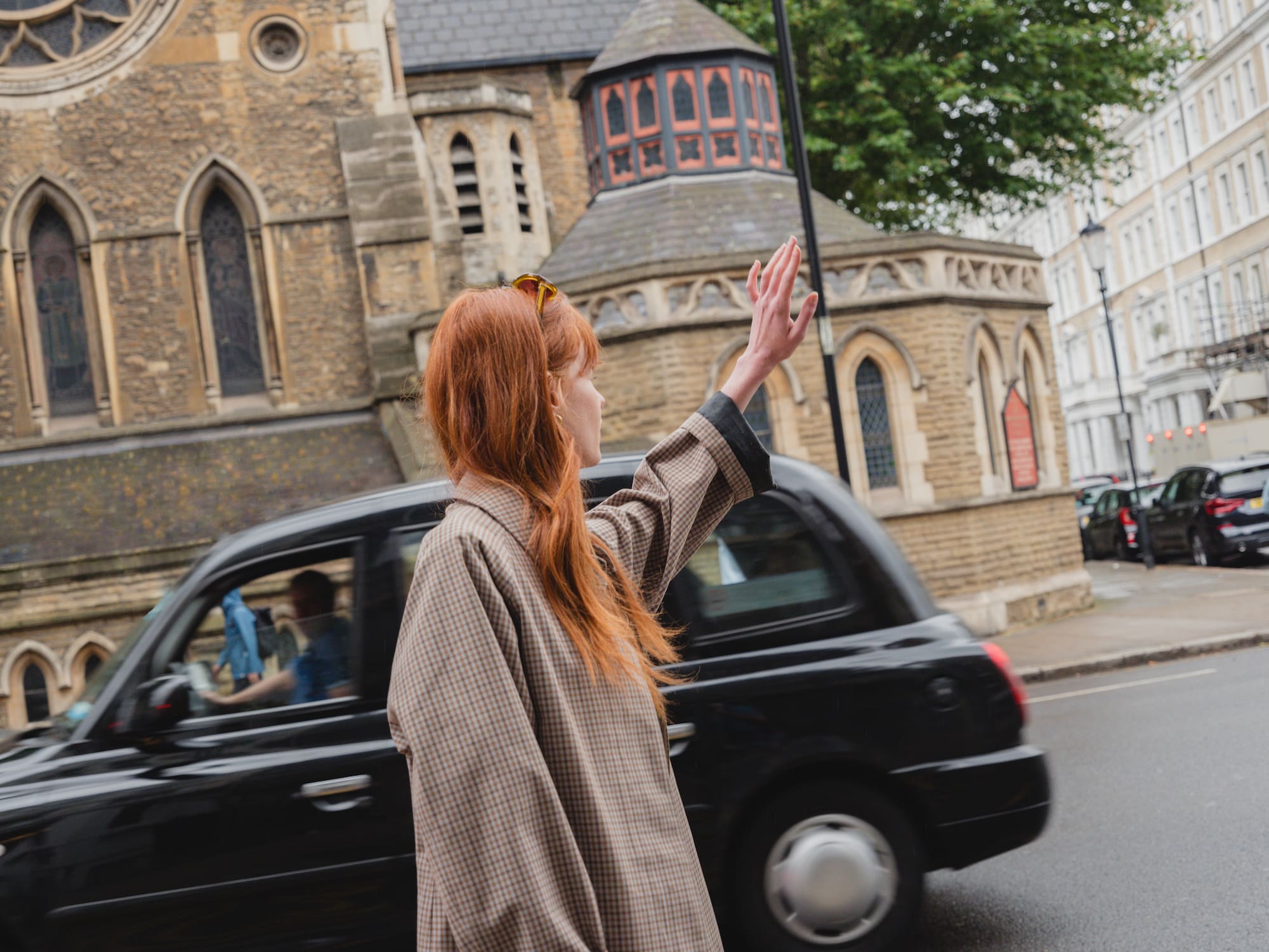 A woman stands on the street next to a black car.
