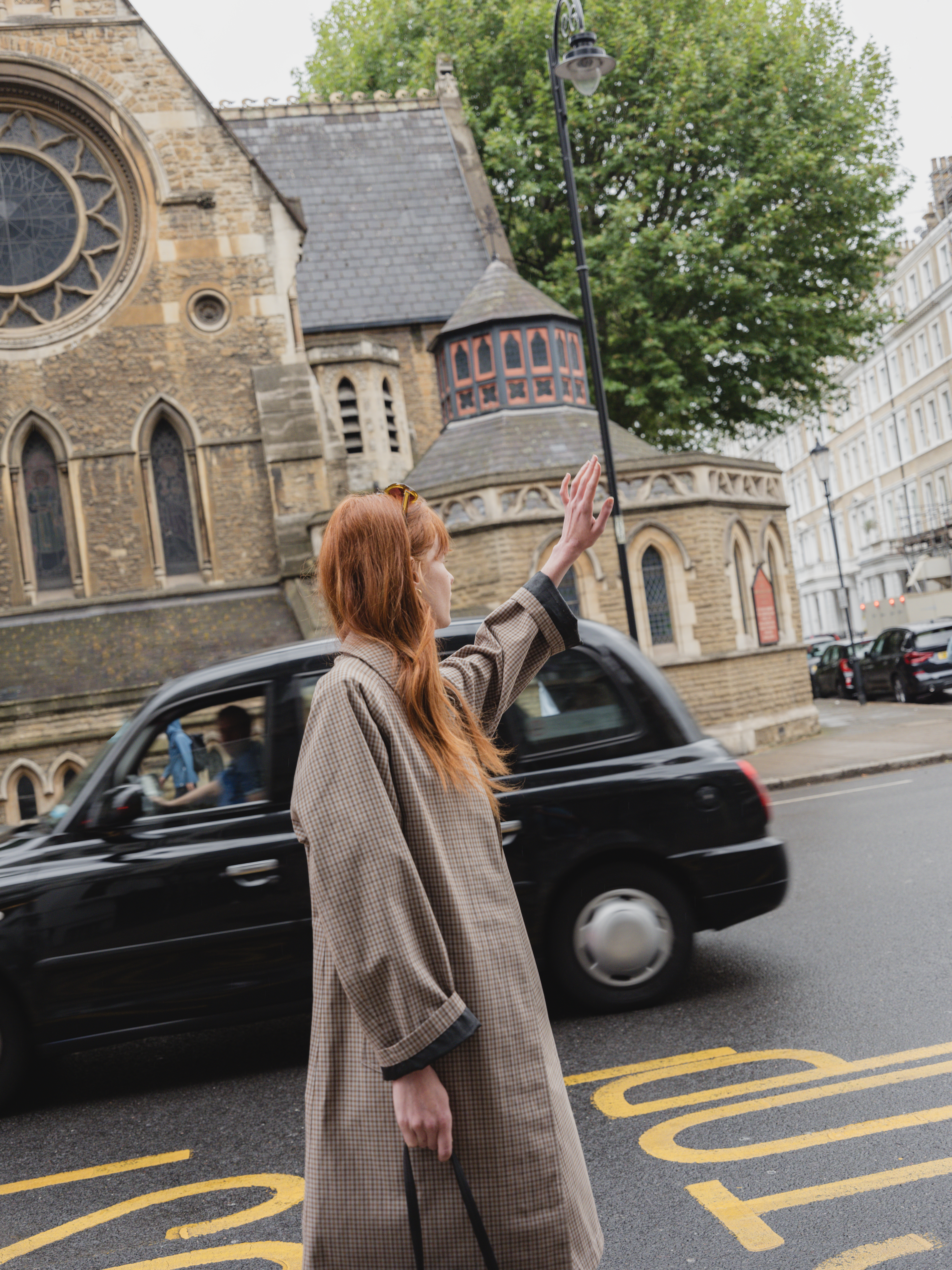 A woman stands on the street next to a black car.