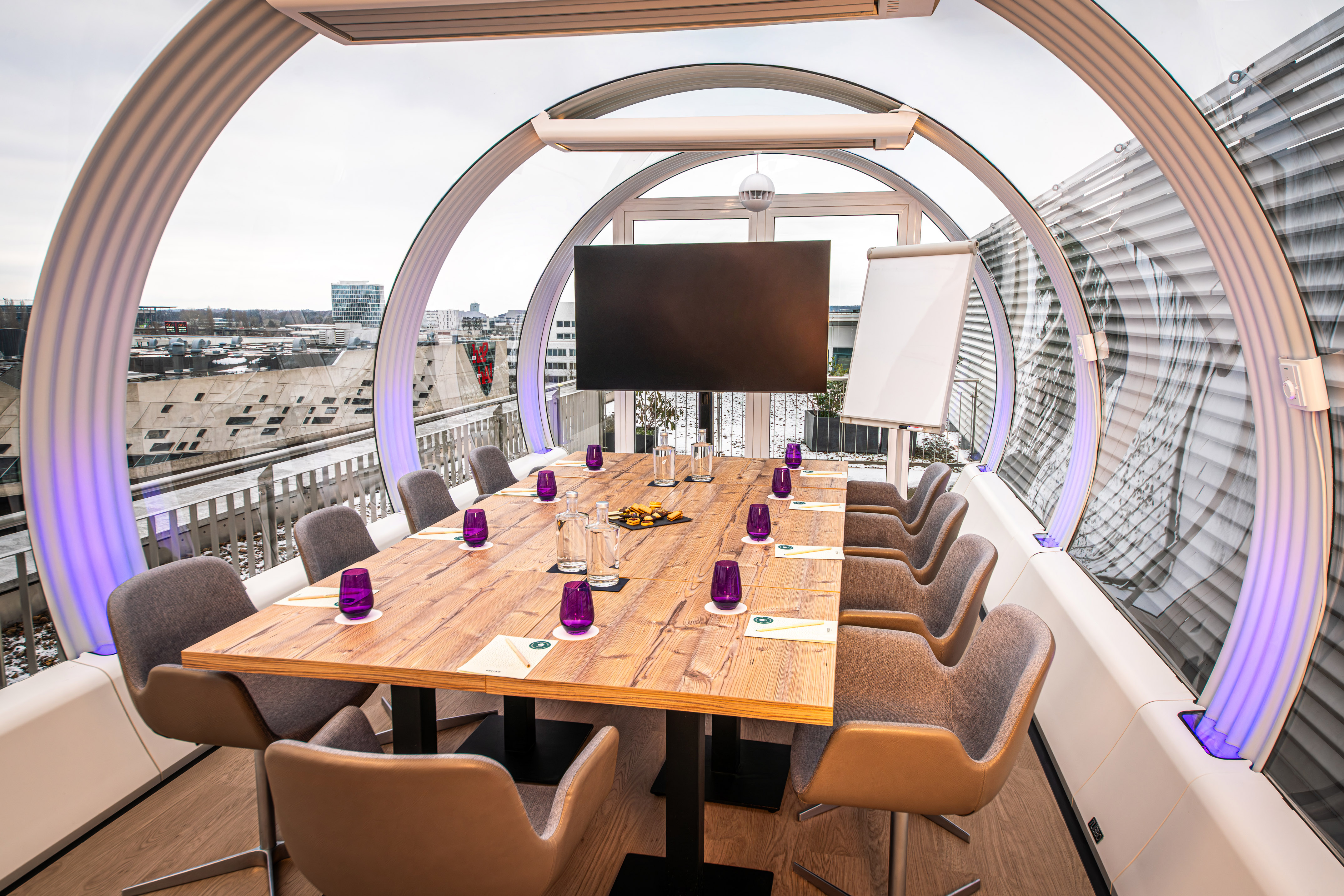Modern rooftop conference room with panoramic city views and large table.