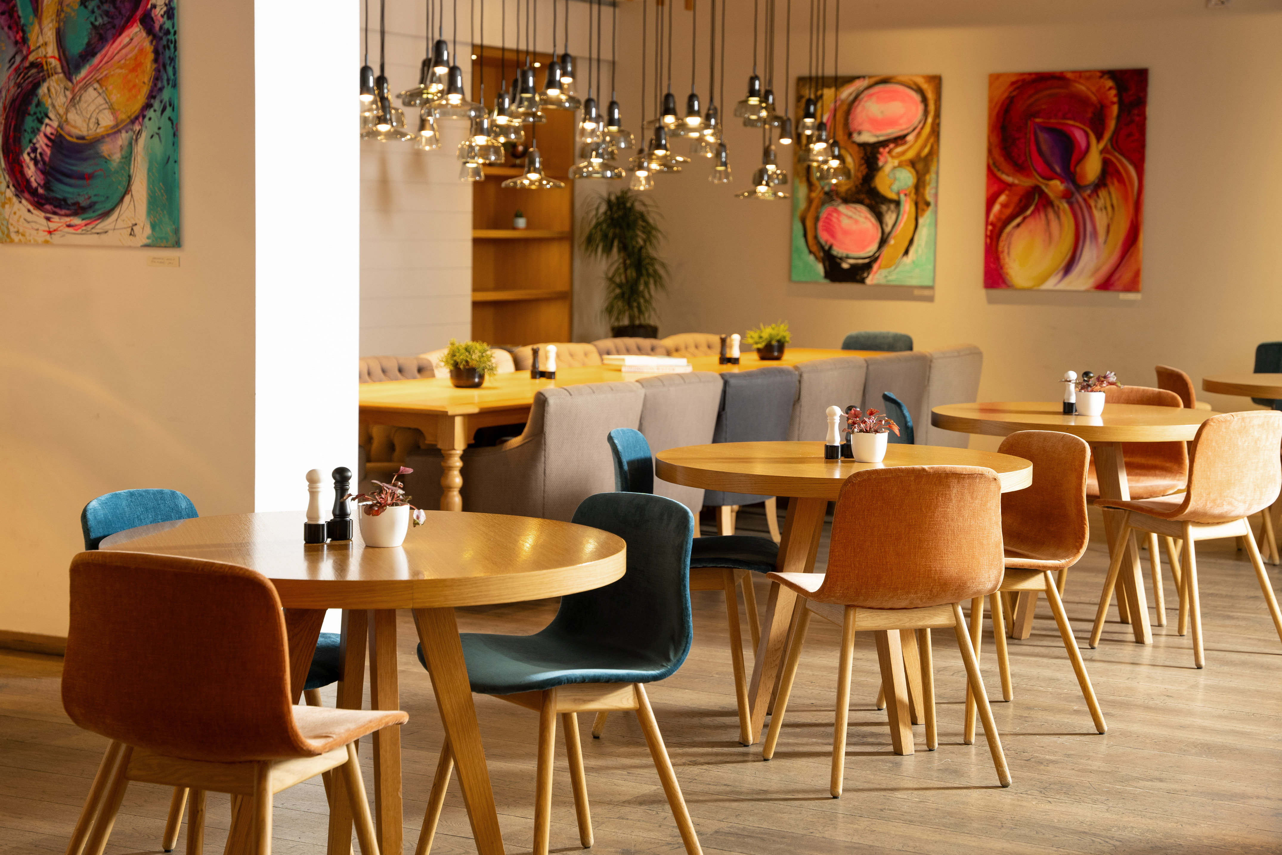 Modern cafe interior with round wooden tables, colorful chairs, abstract art.