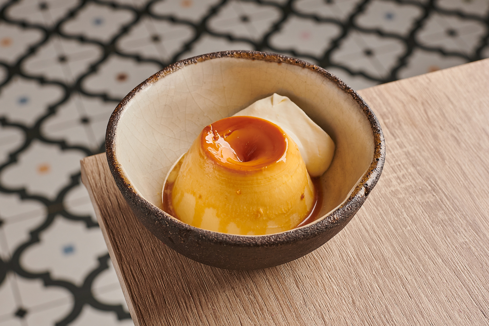 Flan with caramel and cream in a ceramic bowl on a wooden surface.