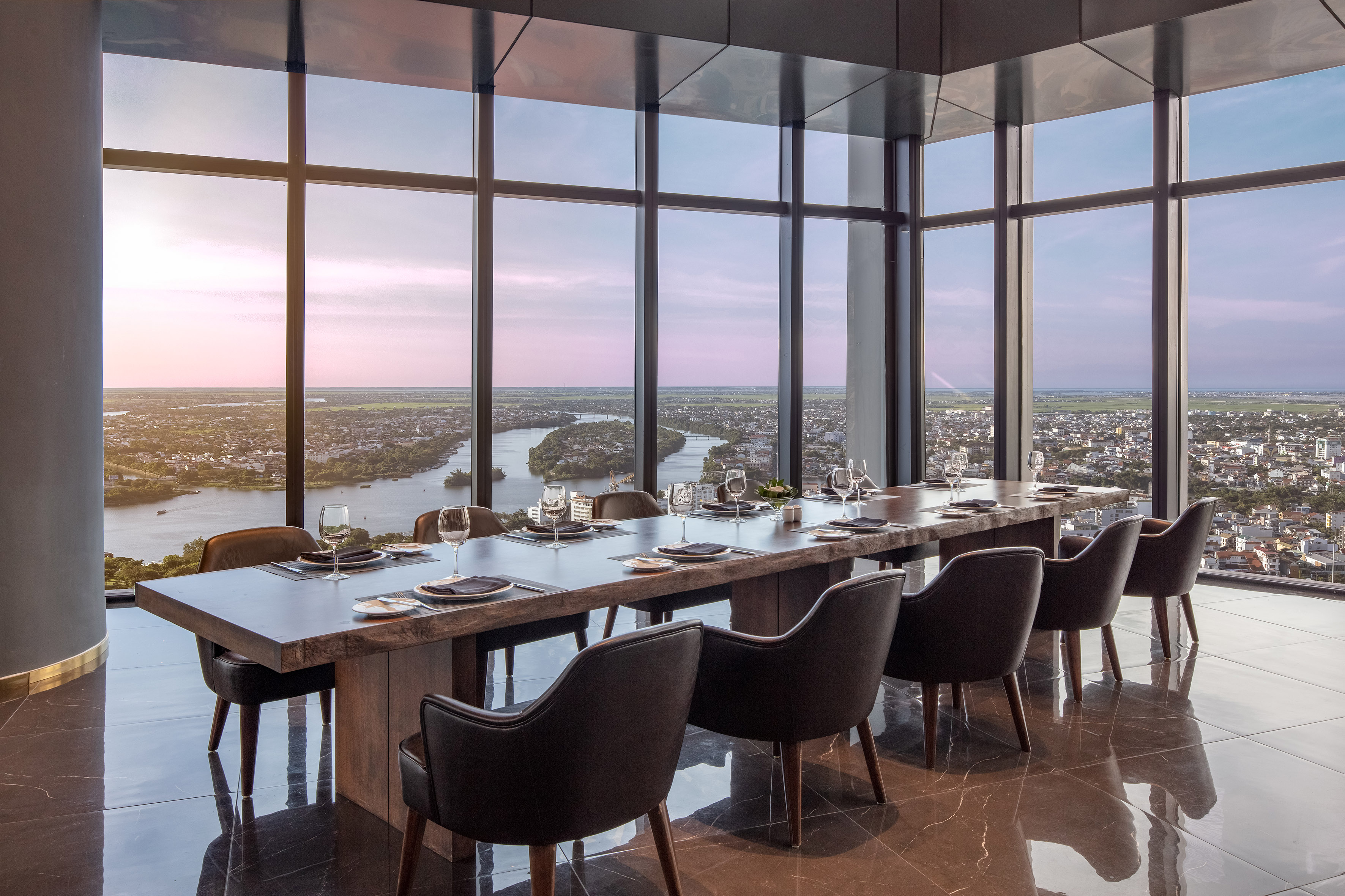 Modern high-rise restaurant dining room, panoramic city river view at sunset.