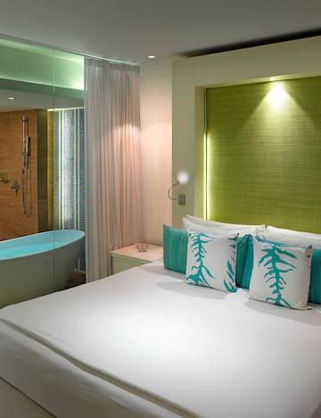 a bed with white sheets and blue pillows in a room with a bathtub