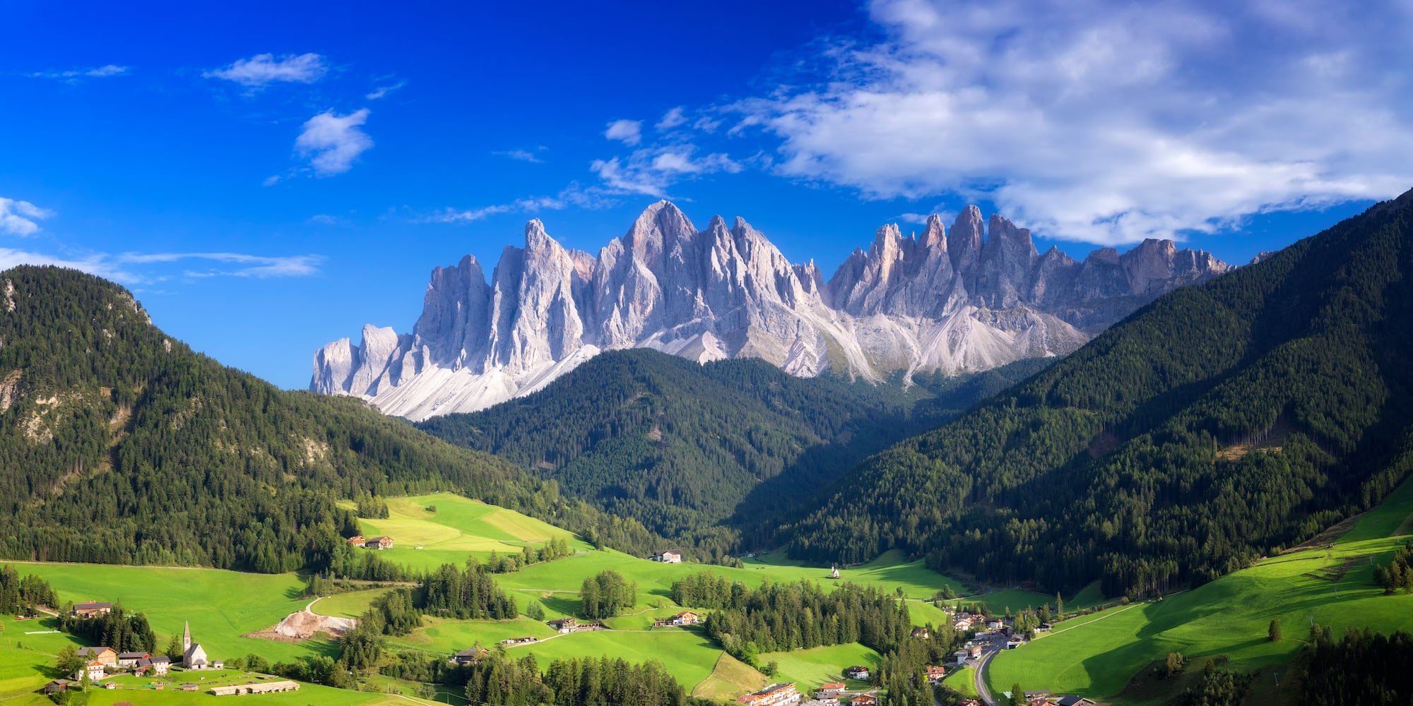 a landscape of green hills and mountains with Dolomites in the background
