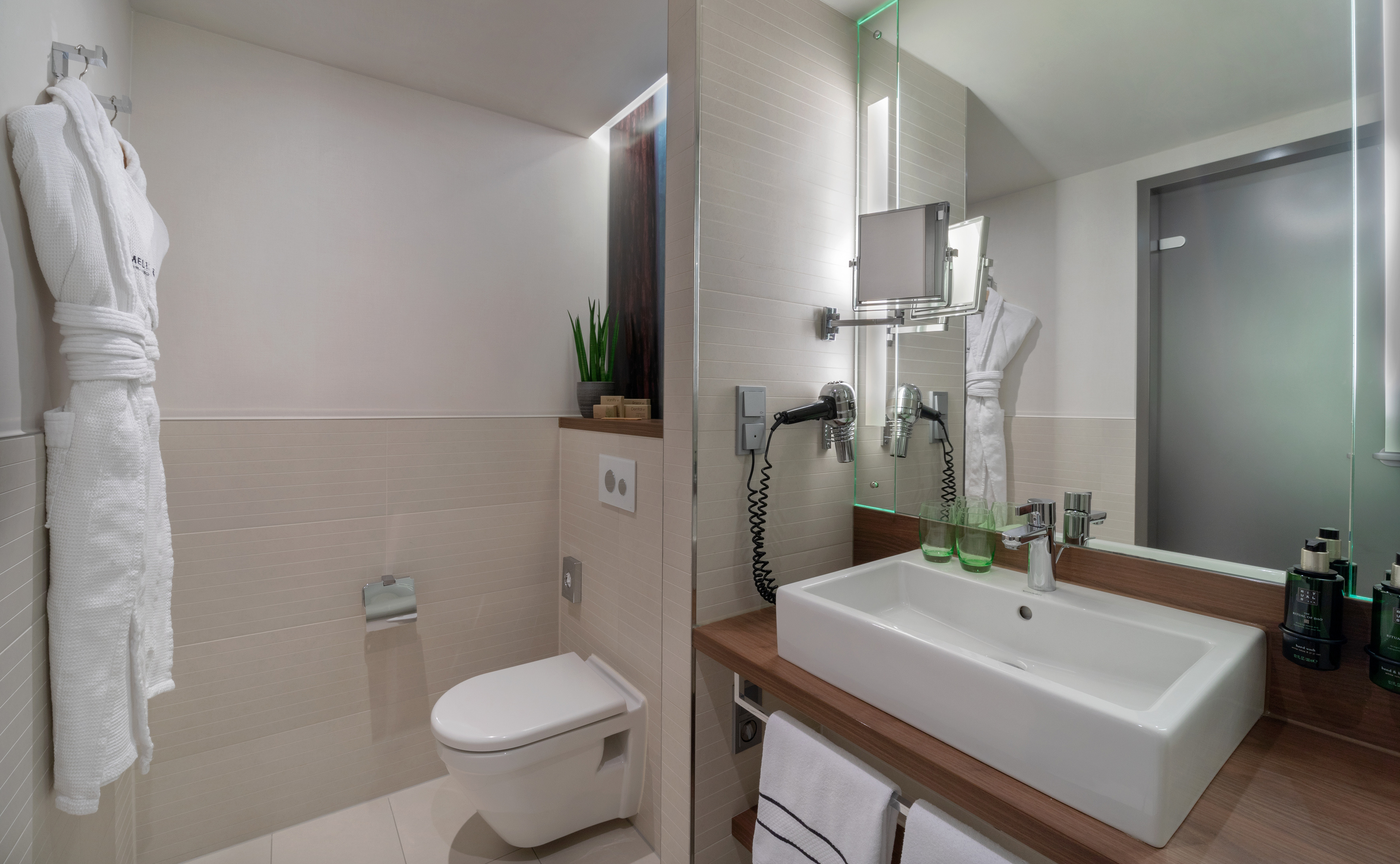Modern bathroom with white bathrobe, toilet, sink, and lighted mirror.