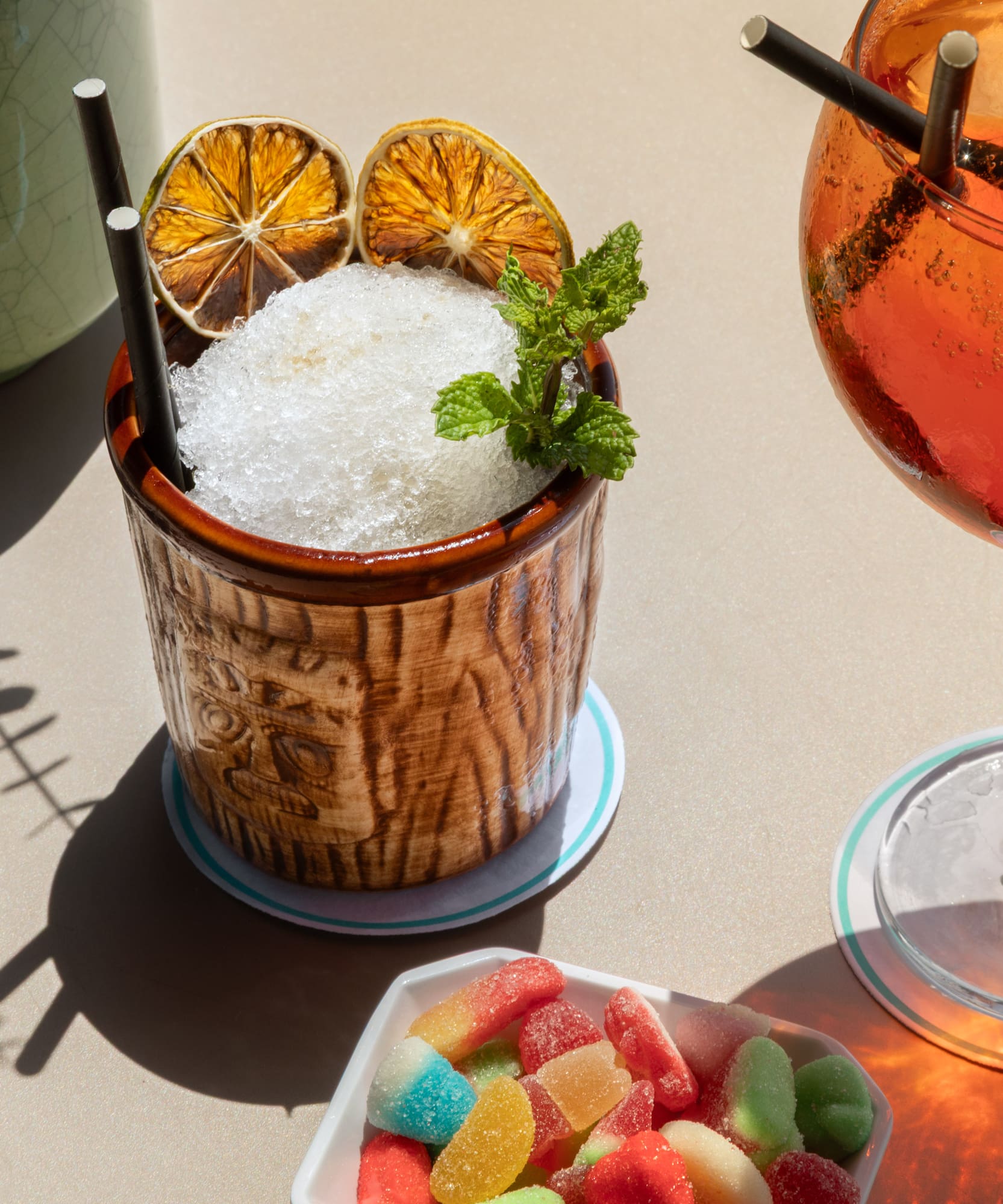Tiki cocktail, Aperol Spritz, and colorful gummy candies on a sunlit table.