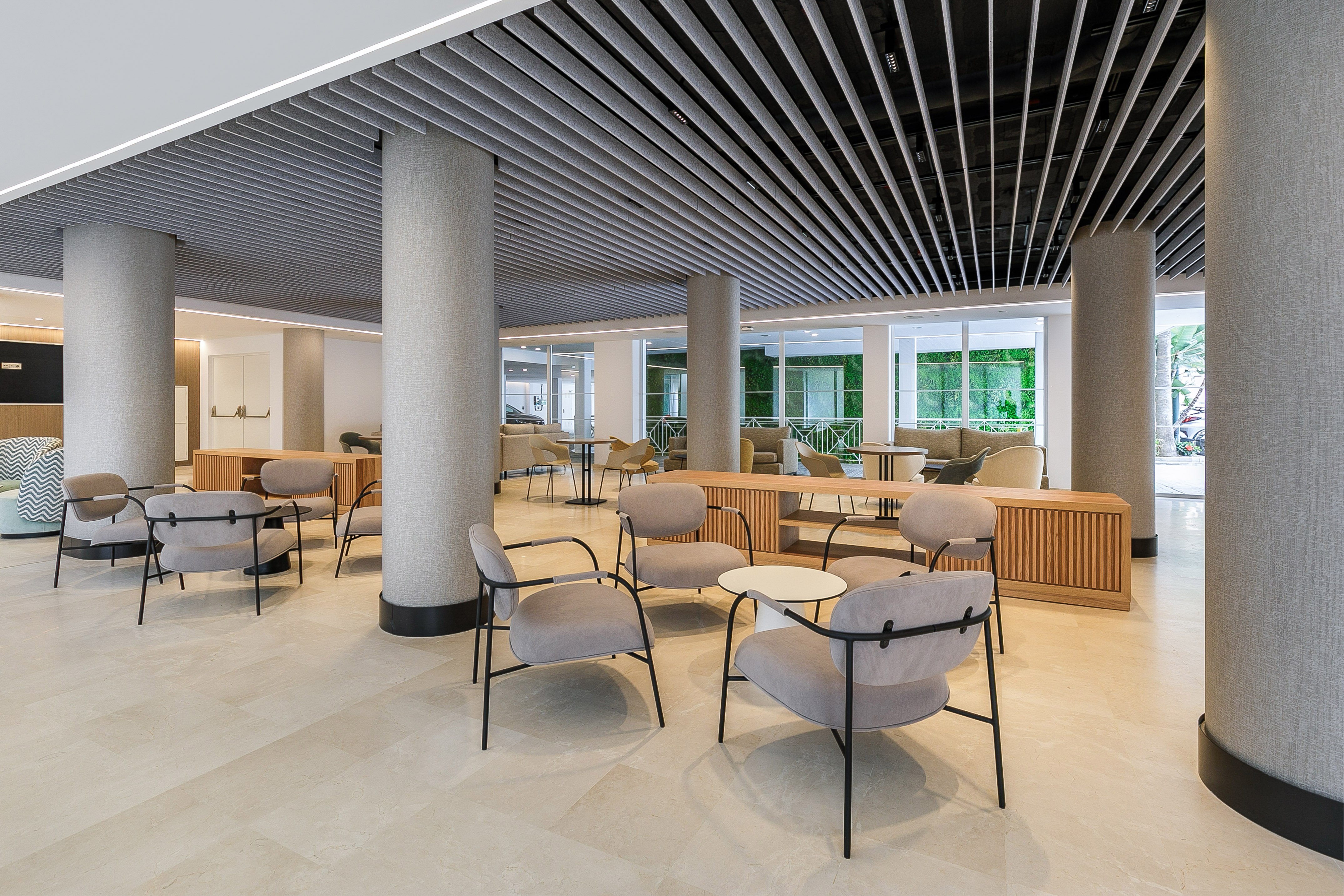 Modern commercial lounge with grey seating, light tiled floor, and slatted ceiling.