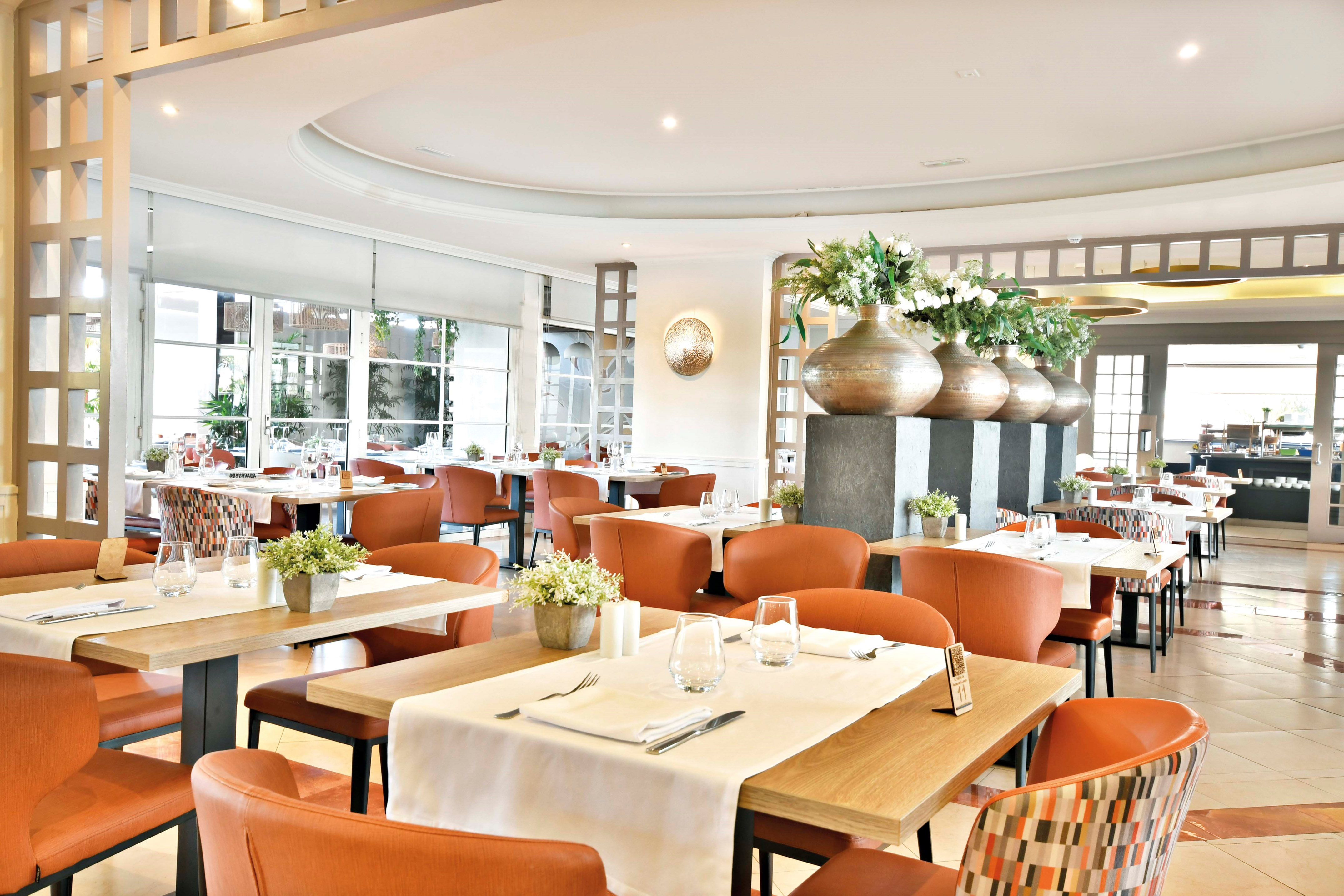 Spacious hotel restaurant dining area with modern orange chairs and buffet.