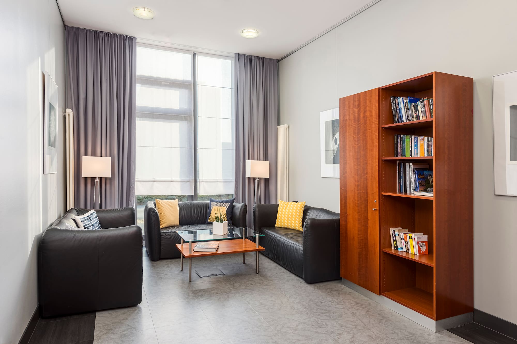 Contemporary lounge with black leather sofas, yellow cushions, wood bookcase.