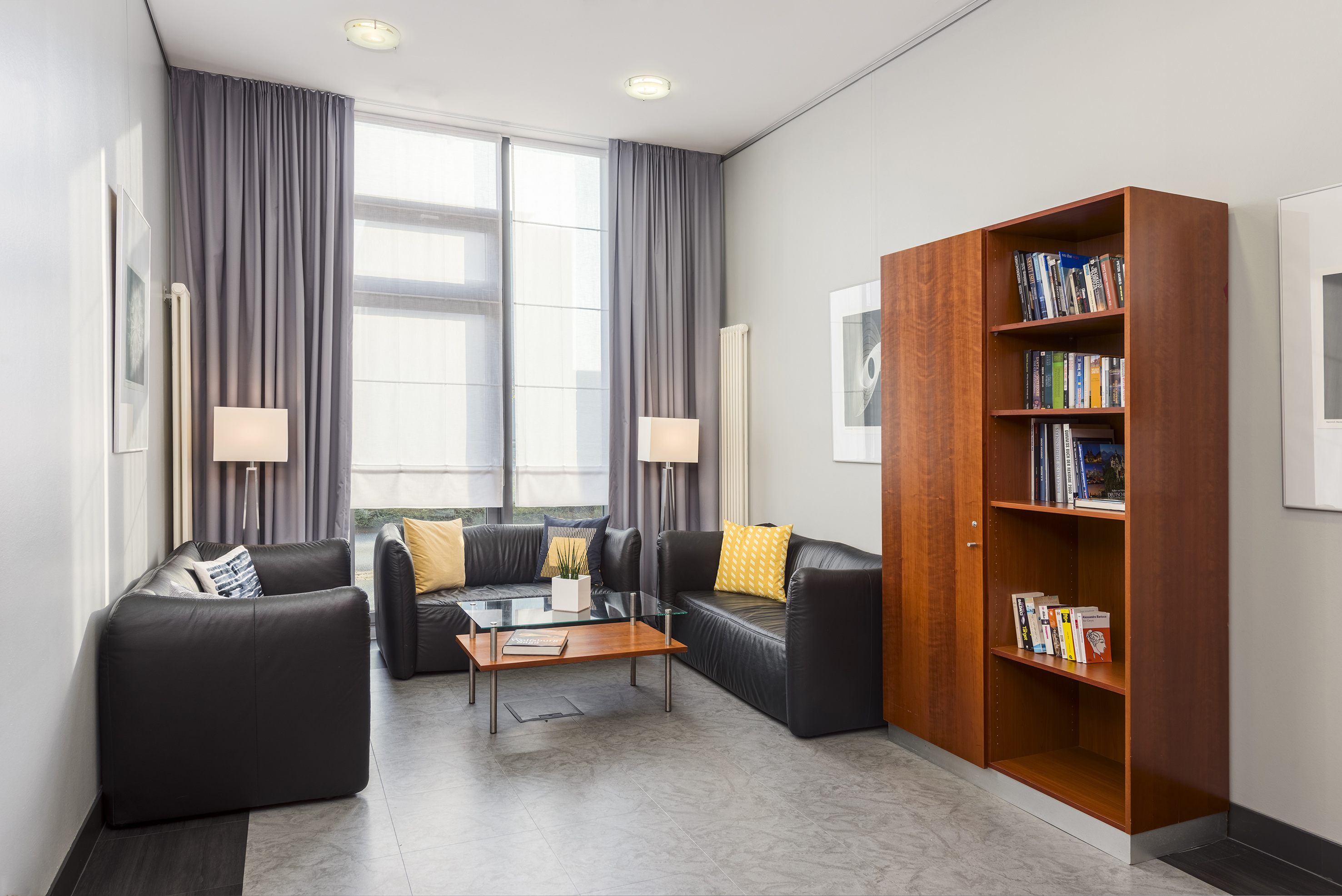 Contemporary lounge with black leather sofas, yellow cushions, wood bookcase.