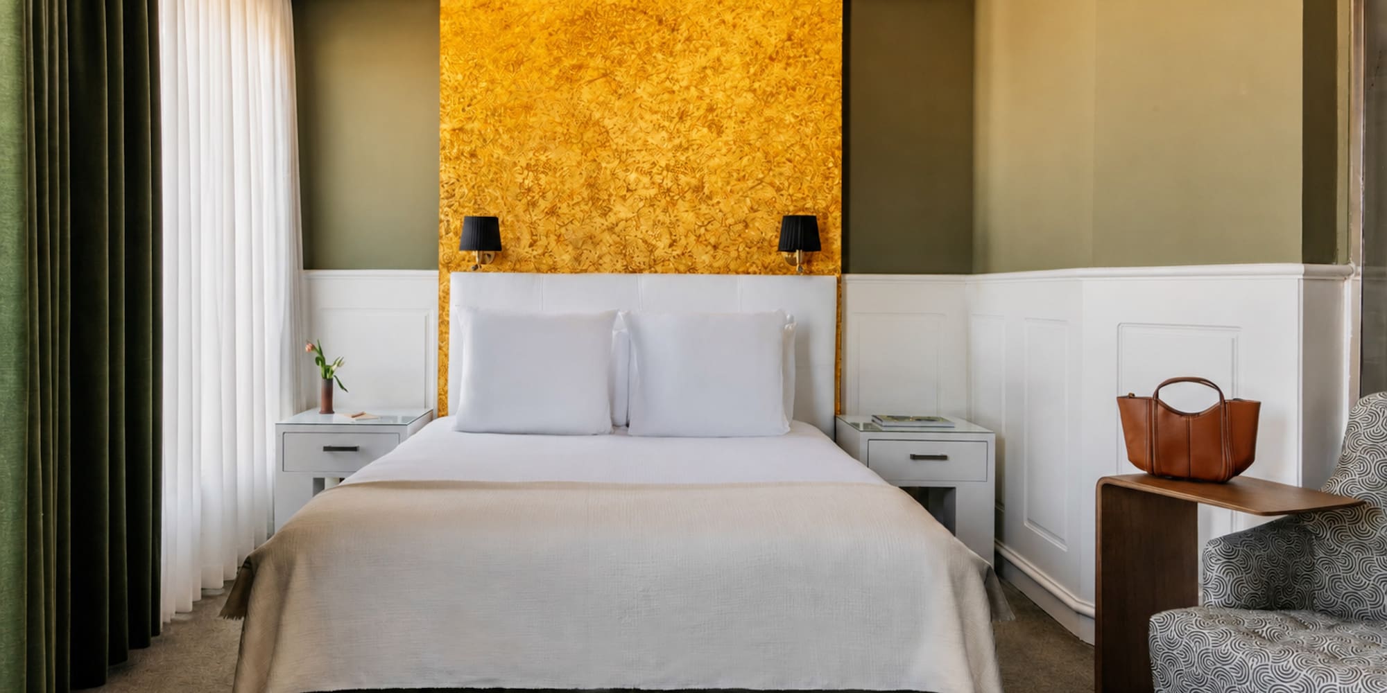 Modern hotel bedroom with gold accent wall, olive green, and white decor.