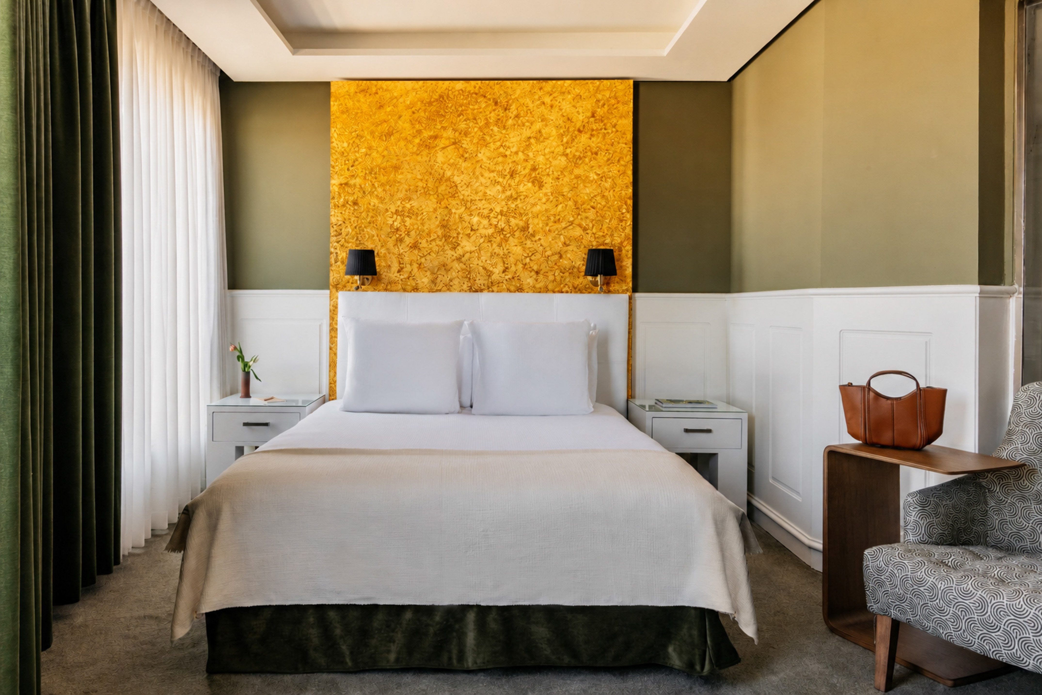Modern hotel bedroom with gold accent wall, olive green, and white decor.