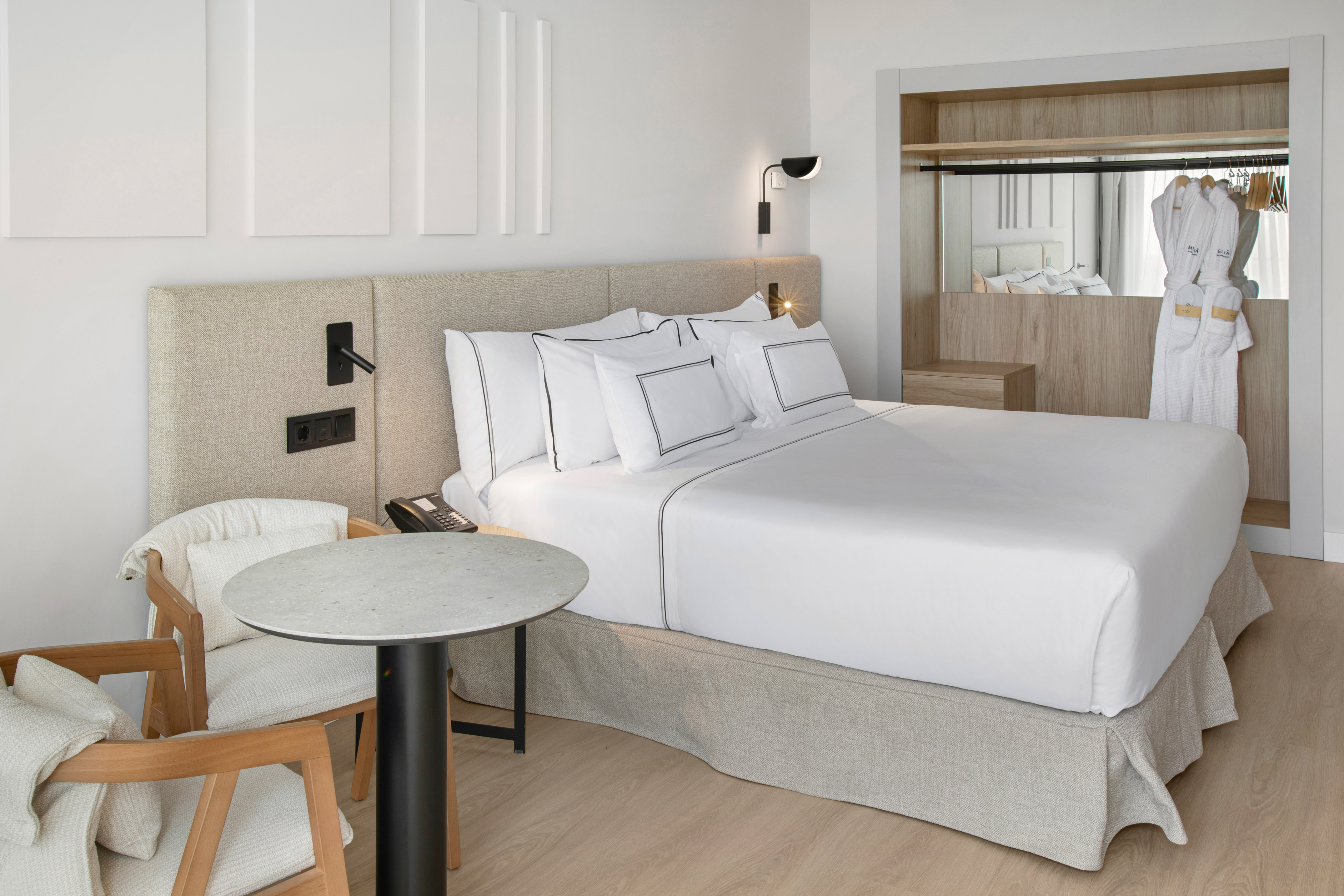 Modern hotel room with large bed, neutral decor, built-in wardrobe, and seating area.
