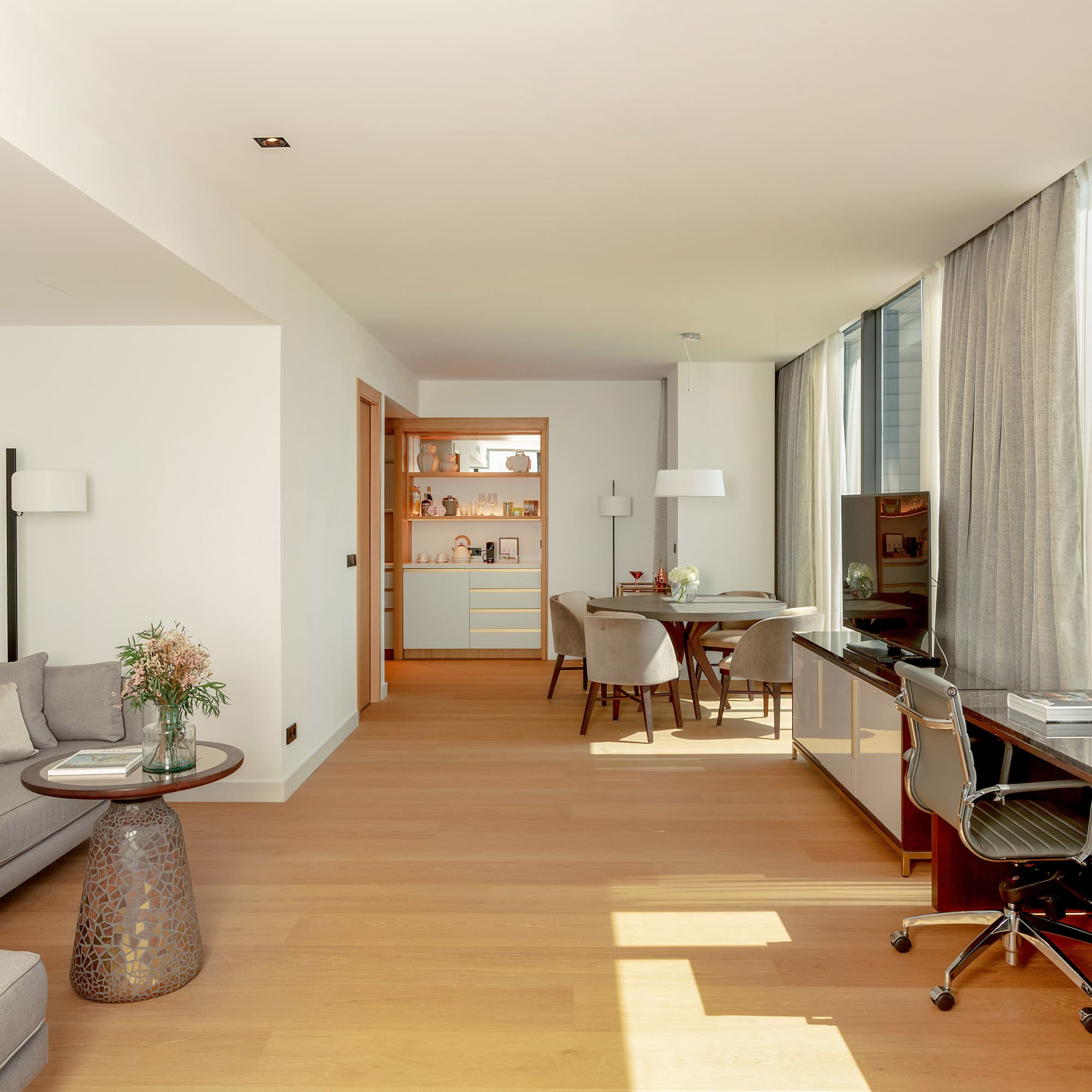 Modern living suite with sofa, dining, desk, hardwood floor, and city view windows.