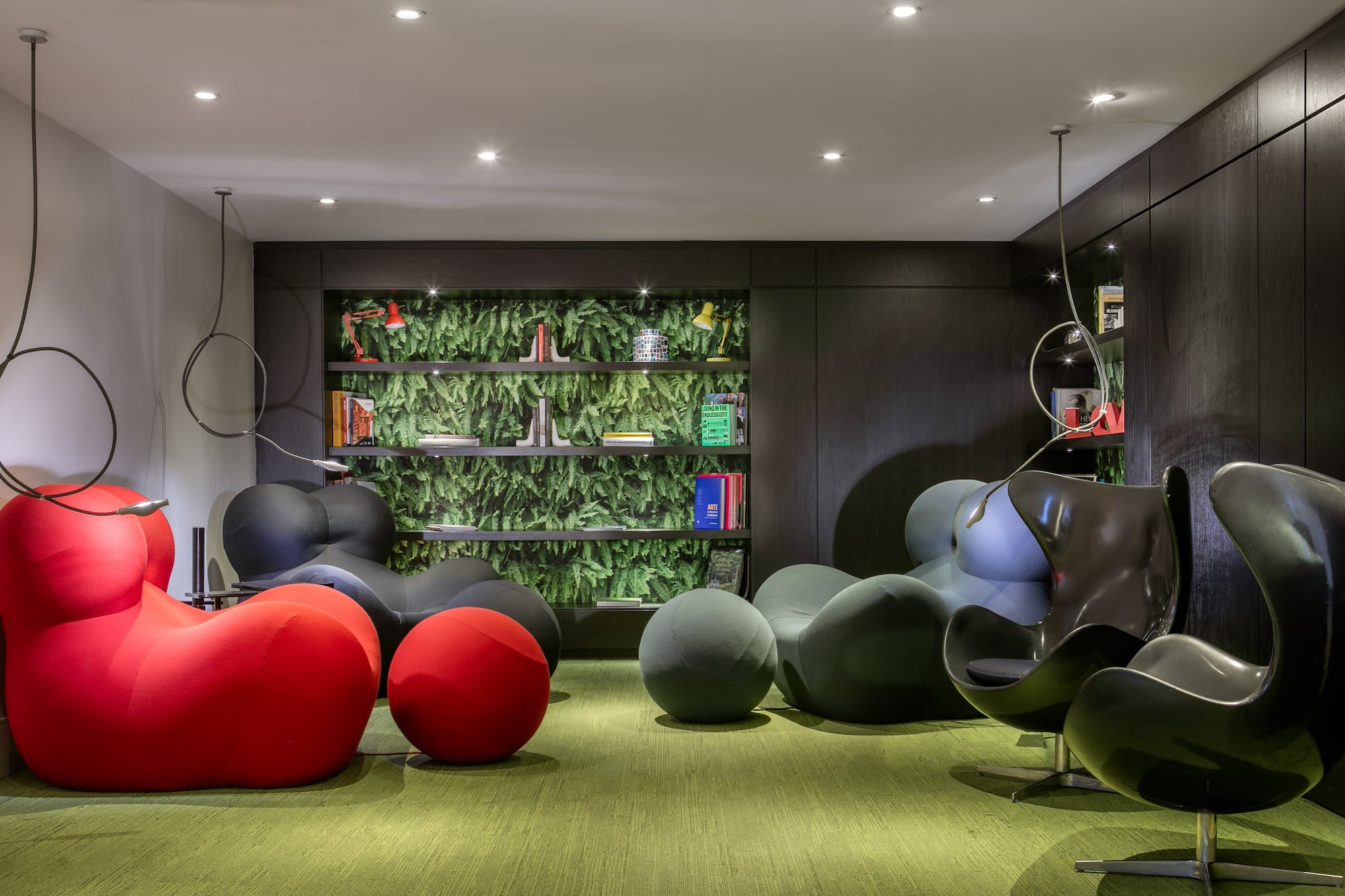 Modern lounge with colorful seating, green carpet, dark wood, and botanical wall shelves.