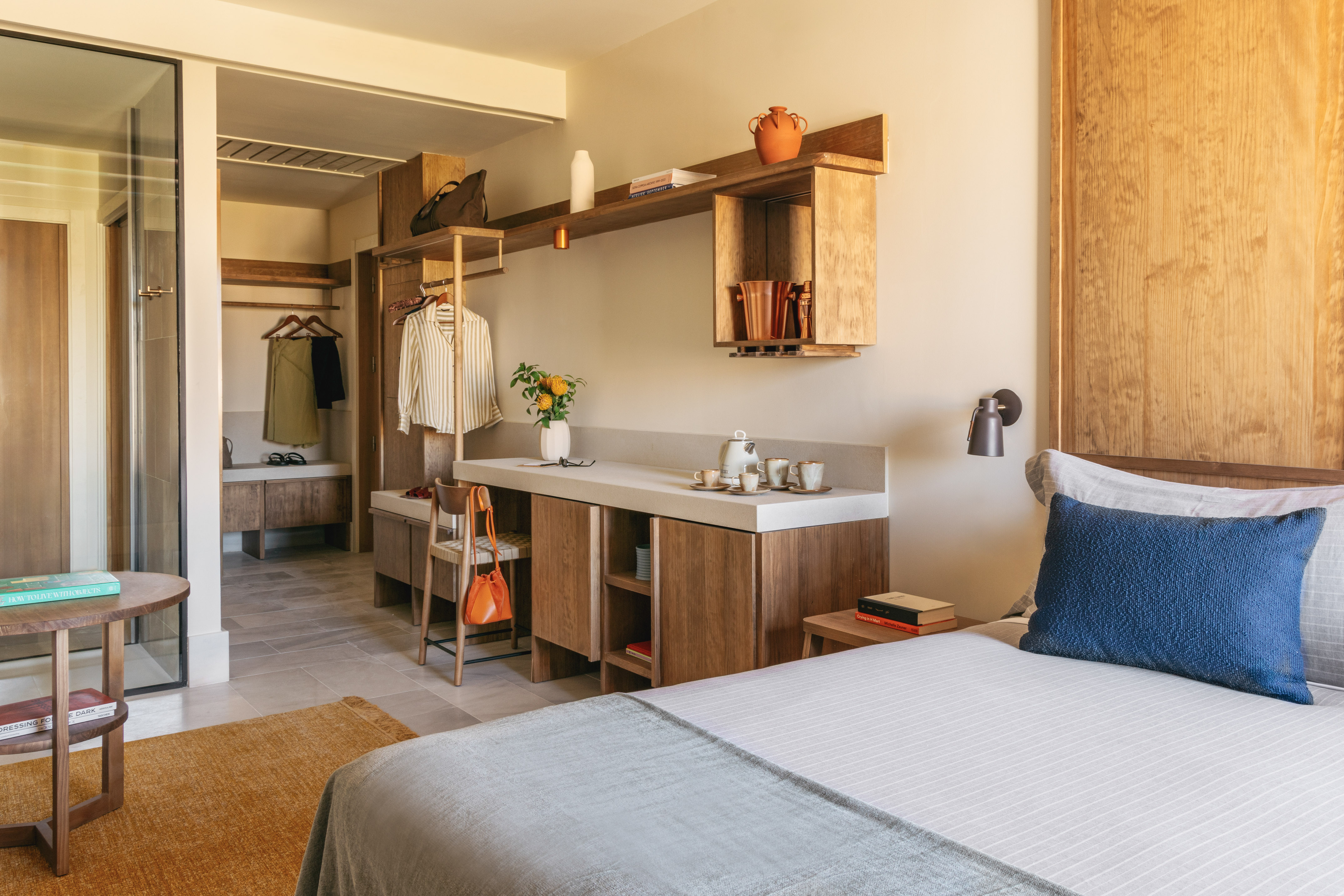 Modern hotel bedroom interior with wooden bed, integrated desk, and open closet.