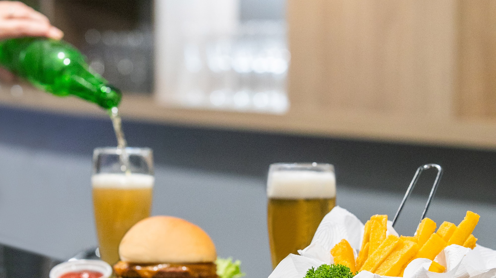 a person pouring a green bottle into a glass of beer on a table with food
