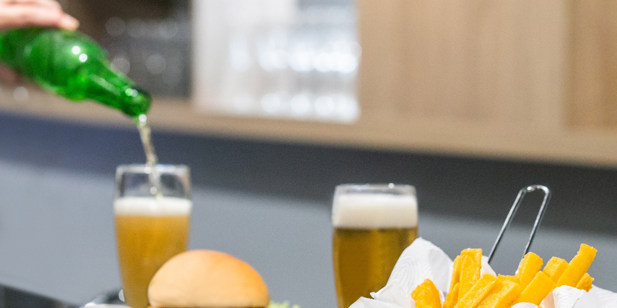 a person pouring a green bottle into a glass of beer on a table with food