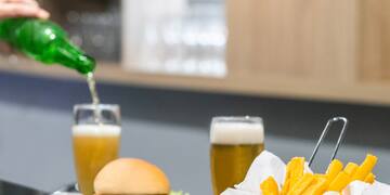 a person pouring a green bottle into a glass of beer on a table with food