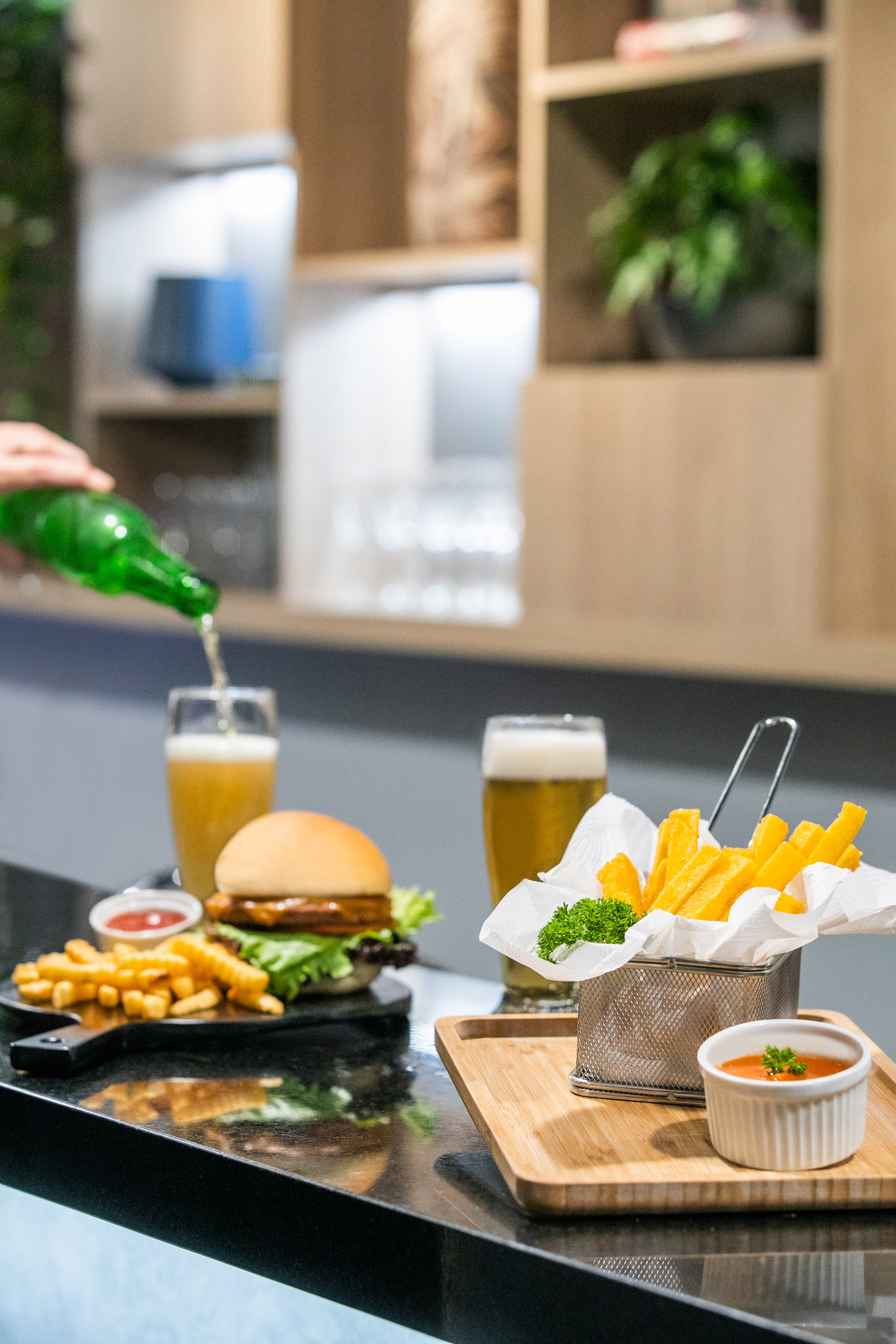 Hand pouring beer, burger, crinkle fries with ketchup, and thick-cut fries with sauce.