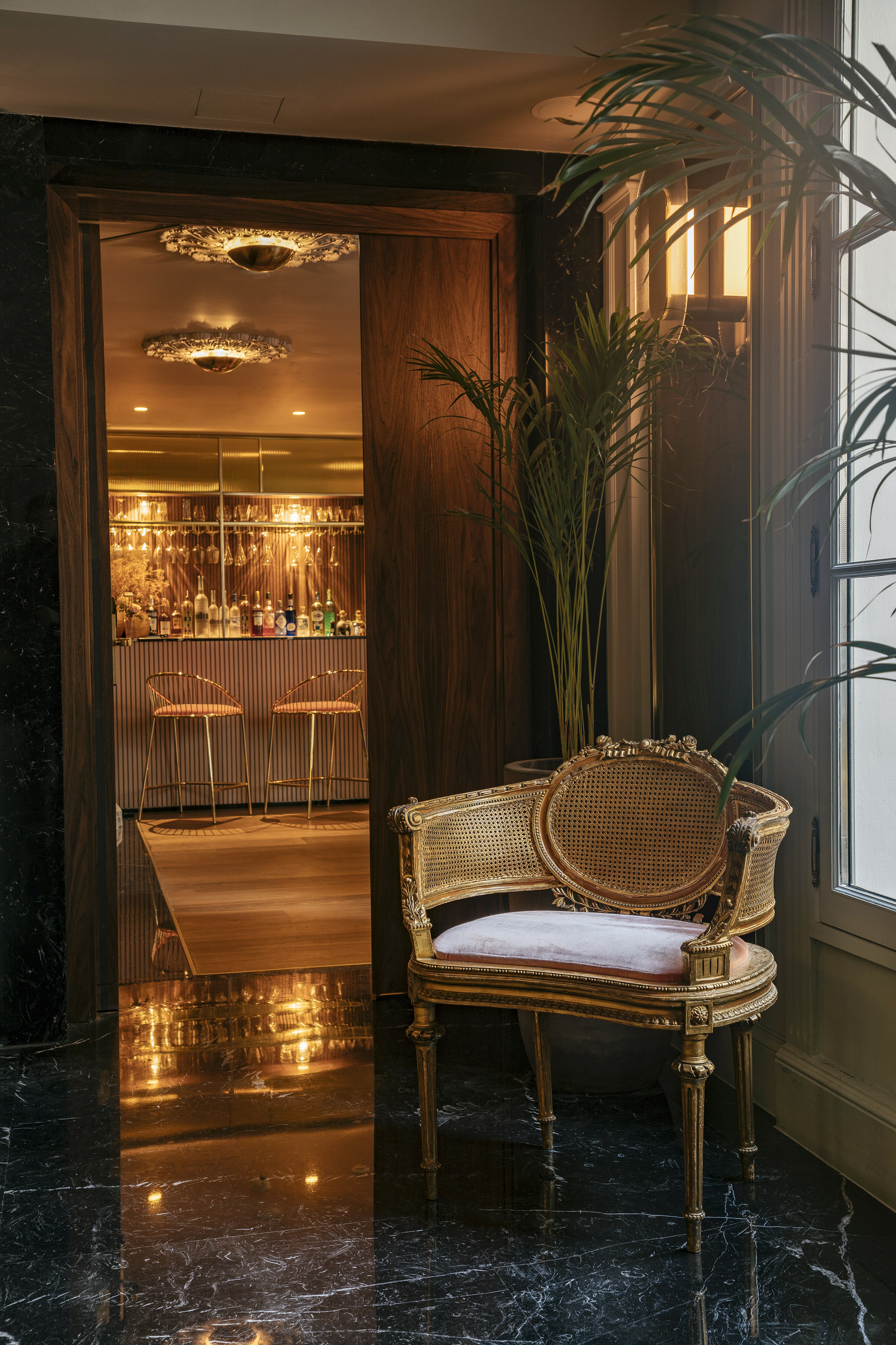 Ornate gold chair by dark marble leading to an opulent cocktail bar entrance.