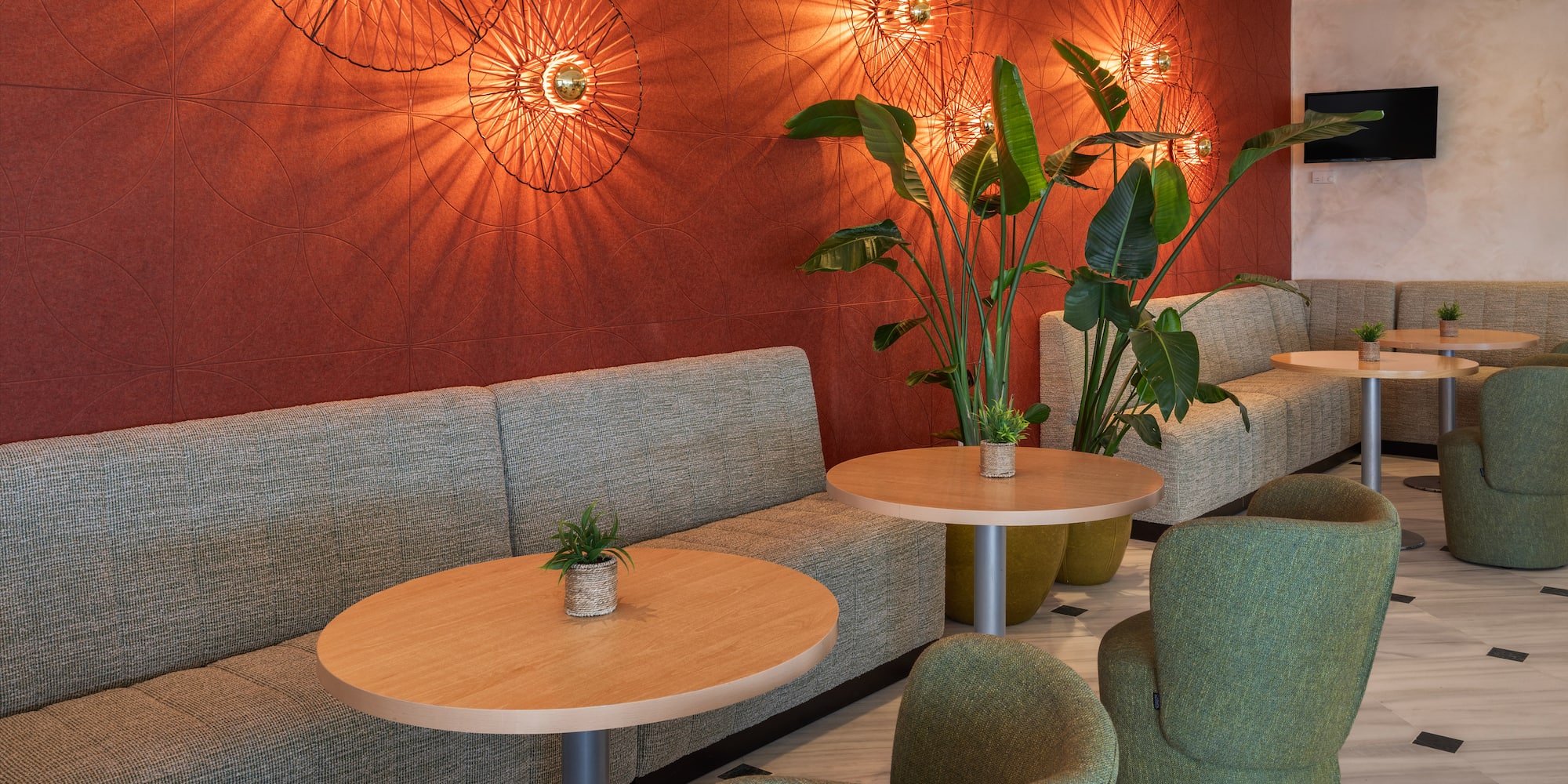 Lobby moderno con sofás, sillones verdes, mesas y pared roja iluminada.
